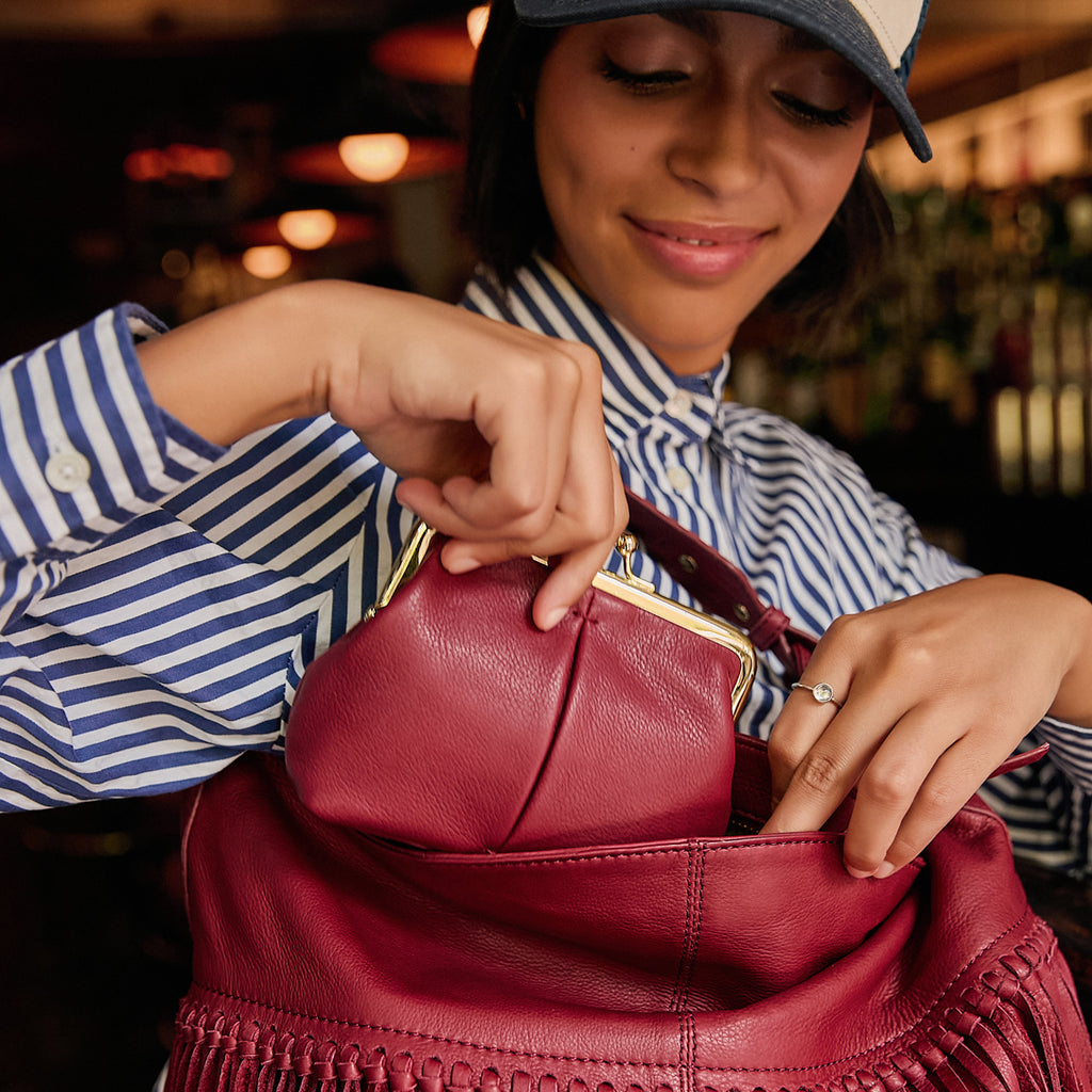 Woman reaching into her bag to pull out the American Leather Co Wolfe Kisslock in dark red.