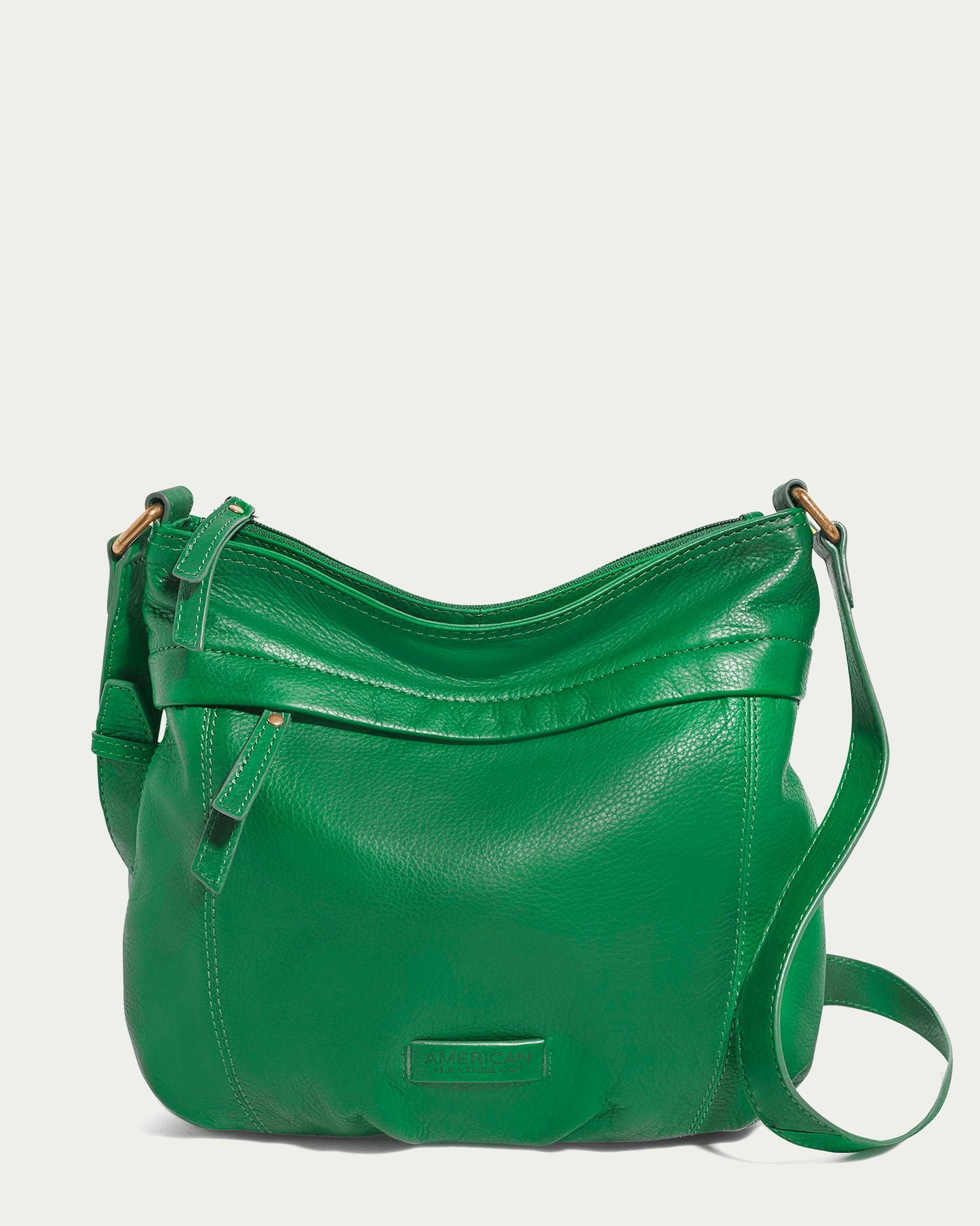 The Acorn Double Entry Crossbody by American Leather Co. is a green leather crossbody bag made from genuine glove leather. It features a top zipper closure, an adjustable shoulder strap, and a small front pocket. The bag showcases simple stitching details and a subtle embossed logo near the bottom.