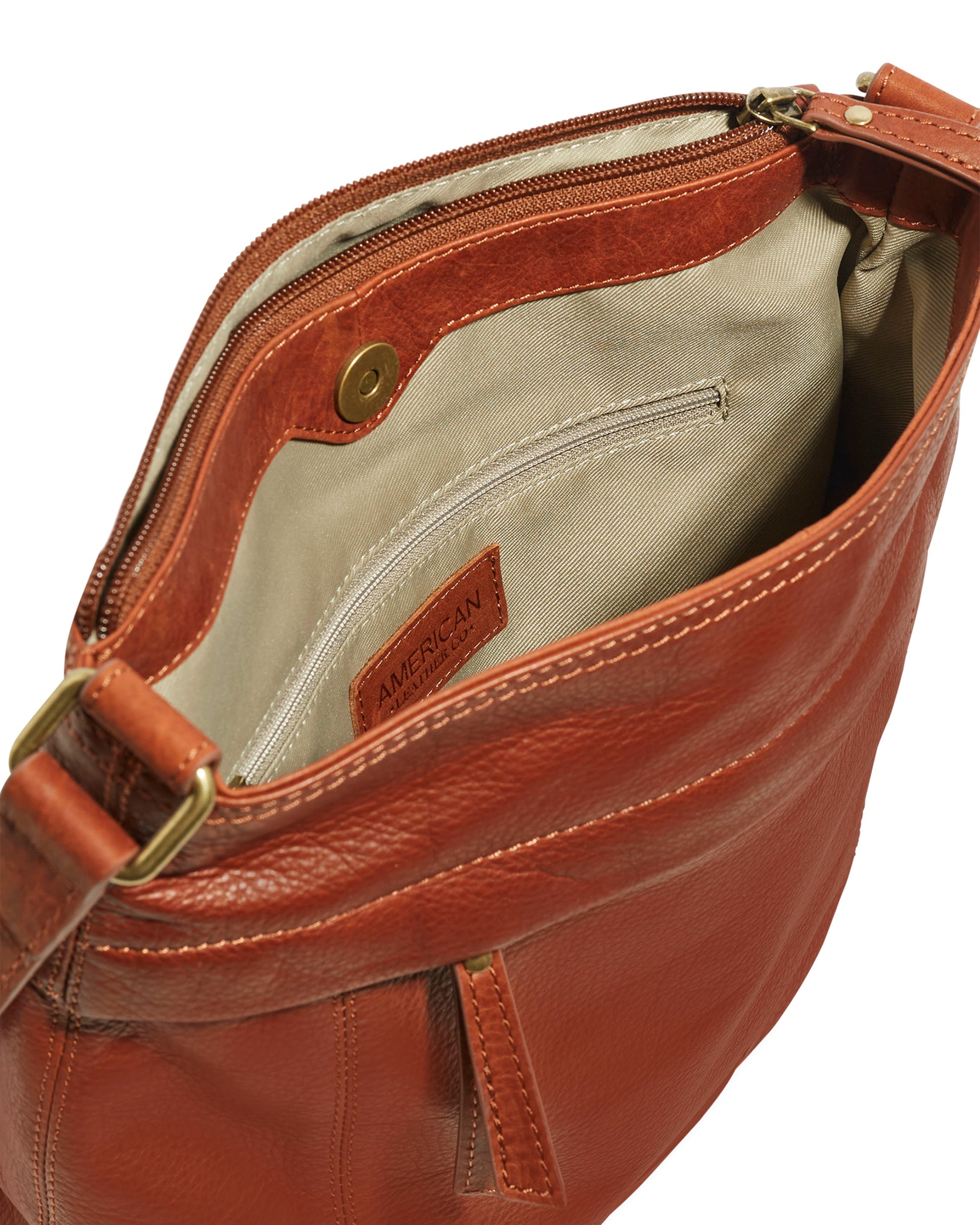 The Acorn Double Entry Crossbody by American Leather Co., crafted from genuine glove leather, is open to reveal its beige fabric interior with a small leather tag. It boasts antiqued hardware, including metal buckles that attach the strap. Inside, there is a zippered pocket, while the outside features a magnetic closure.