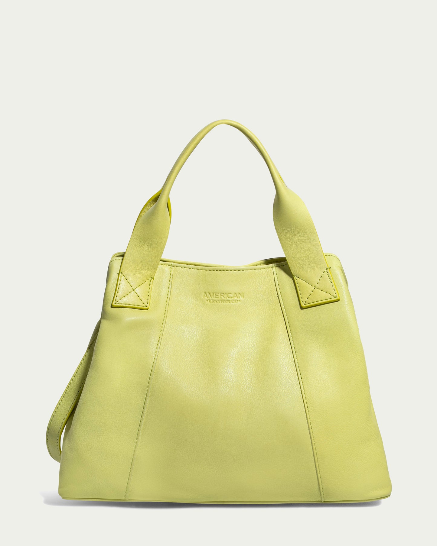 The Ada Triple Entry Satchel from American Leather Co. is a lime green leather tote bag that includes two short handles and an adjustable crossbody strap. Made from genuine American leather, it showcases stitched detailing with the brand name embossed on the front. This bag's clean, minimalist design effortlessly complements any outfit.