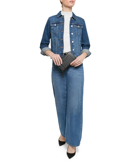 A person wears a denim jacket, wide-leg jeans, and a white top. In the left hand pocket is the Austin Continental Wallet with RFID from American Leather Co. They pair this look with a small black clutch and pointed-toe shoes against a plain white background.