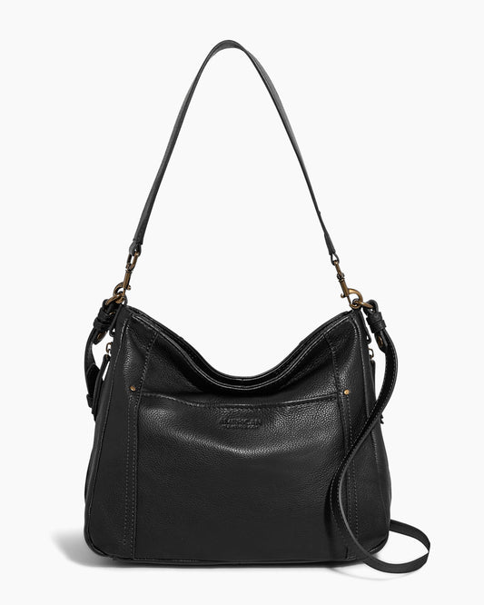 The Austin Convertible Shoulder Crossbody by American Leather Co. is a black leather bag with a slouchy design and a slightly curved top. It features a single, adjustable shoulder strap attached with silver hardware, side zipper pockets for added convenience, and includes an additional long, detachable cross-body strap. The bag has minimal detailing and offers a simple, elegant look.