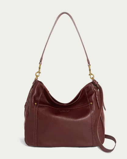 The Austin Convertible Shoulder Crossbody by American Leather Co. is a refined and versatile accessory for everyday use. Crafted in brown leather with a pebbled texture, it features gold-tone hardware, a spacious main compartment, side zipper pockets, and a curved silhouette. This bag also includes a detachable shoulder strap for easy conversion to suit your needs.