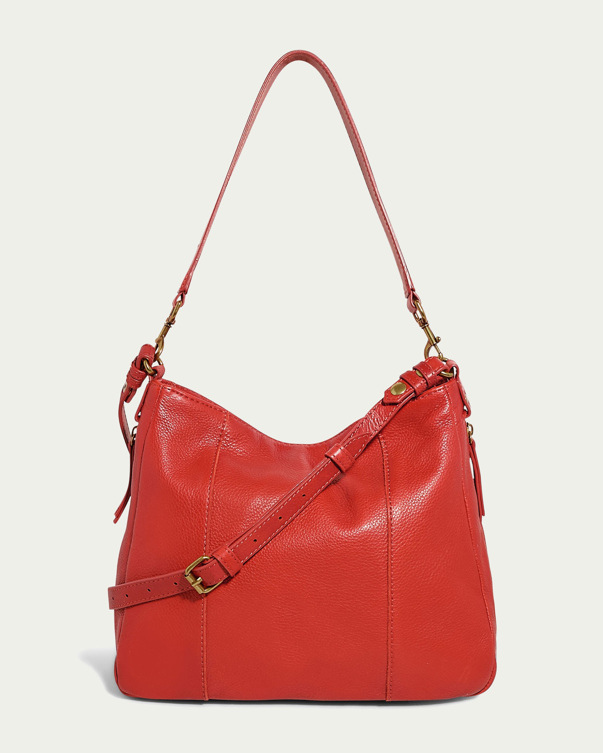 Introducing the Austin Convertible Shoulder Crossbody from American Leather Co. This stylish red leather crossbody bag, adorned with gold-toned hardware, features a long shoulder strap and an adjustable crossbody strap for added convenience. It also includes practical side zipper pockets. The bag boasts a smooth, glossy finish and a sleek, modern design.