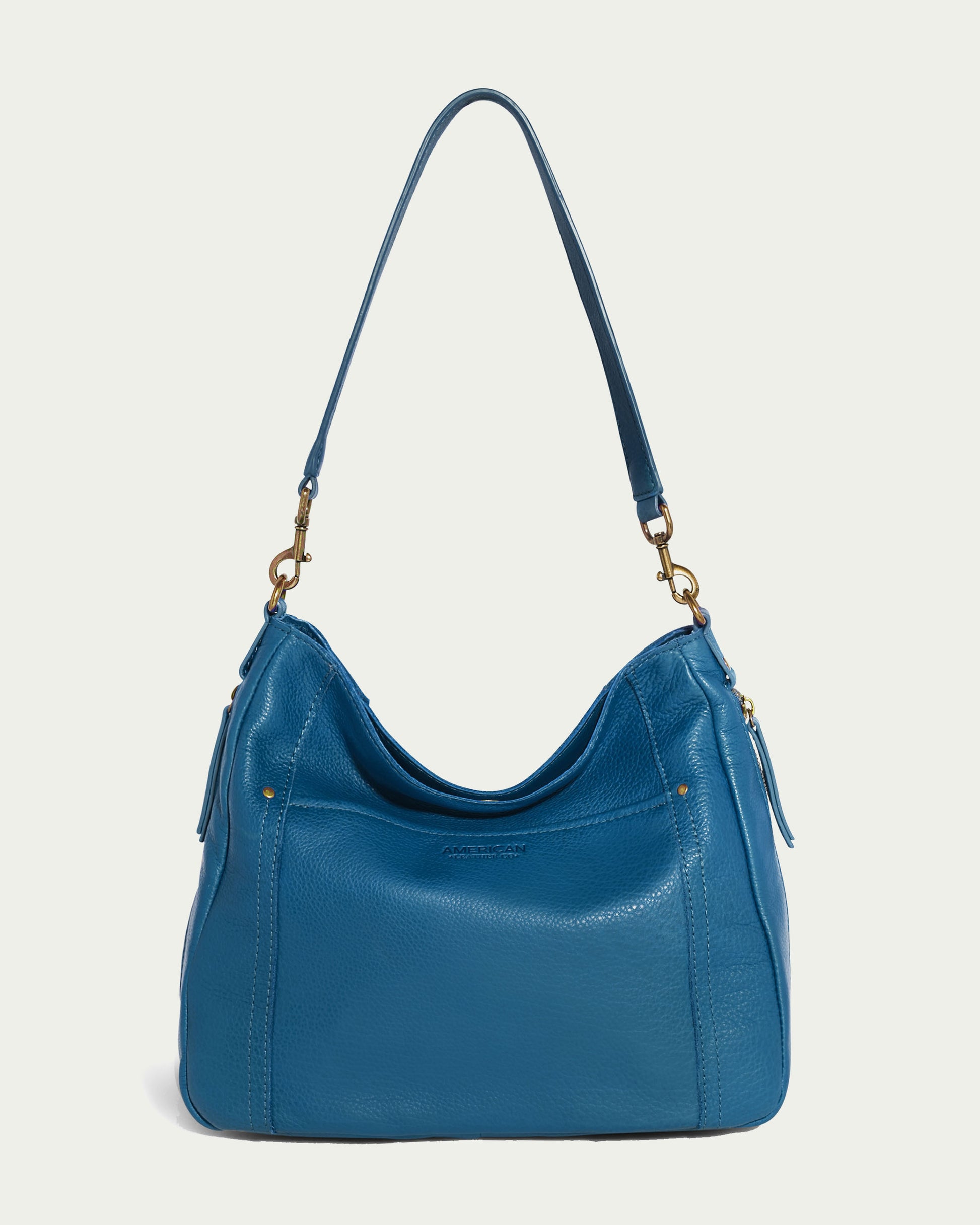 The Austin Shoulder bag from American Leather Co. is a stylish blue handbag made from genuine American leather, featuring a curved top and a long strap. This casual accessory is adorned with gold-tone hardware, including clasps on both ends, and showcases subtle stitch detailing.