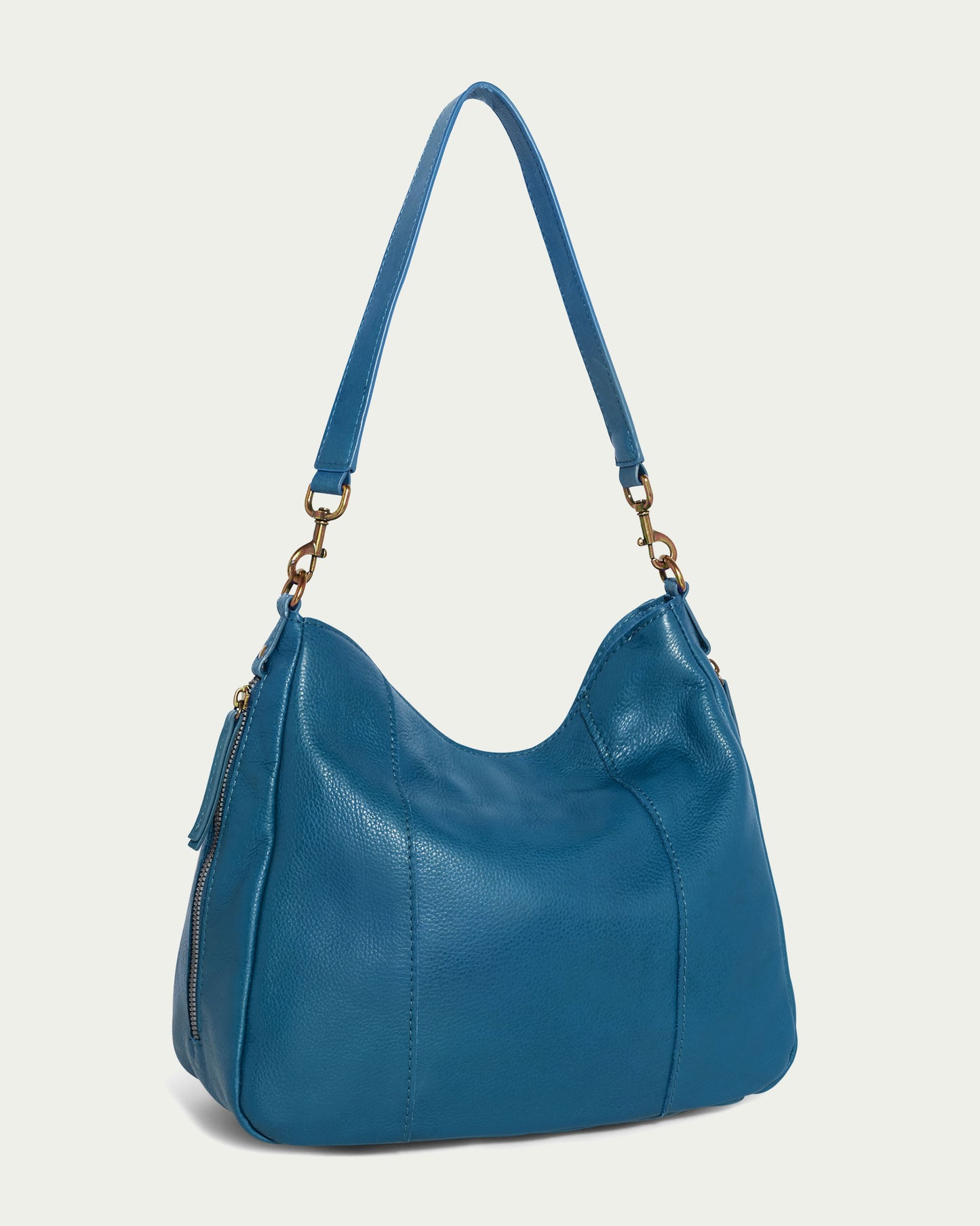 The Austin Shoulder from American Leather Co. is a chic blue leather handbag crafted from genuine American leather. It boasts a curved top design, shoulder strap, and gold hardware accents. This casual accessory features a side zipper pocket and smooth texture, with simple stitching that embodies a modern and sophisticated appearance.