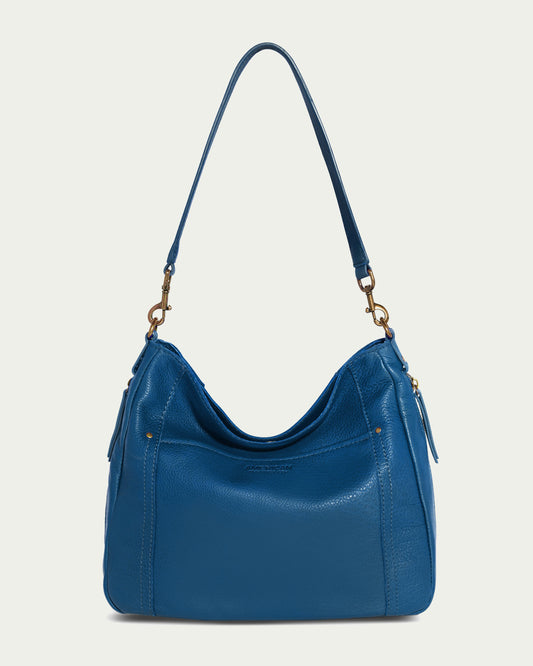 The Austin Shoulder bag from American Leather Co. is a blue leather handbag made from genuine American leather, featuring gold-tone hardware and a shoulder strap. It showcases a slouchy, hobo style with subtle stitching details and a front clasp for added elegance.