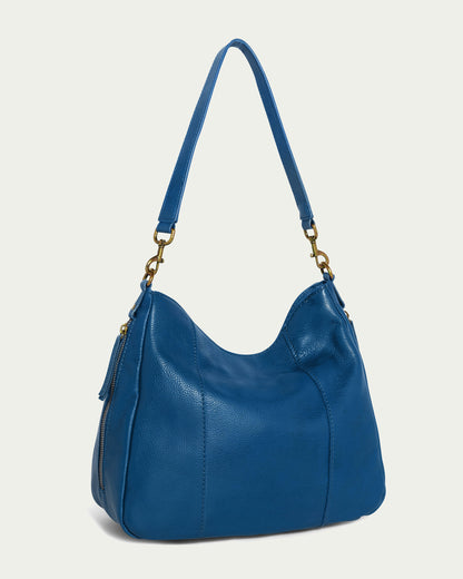 The Austin Shoulder from American Leather Co. is a chic handbag made from genuine American leather in a rich deep blue hue. It features a curved top design and a convenient shoulder strap, accented by eye-catching gold-tone hardware including side buckles and zipper pulls. The bag's surface showcases subtle stitching details that add an elegant touch.