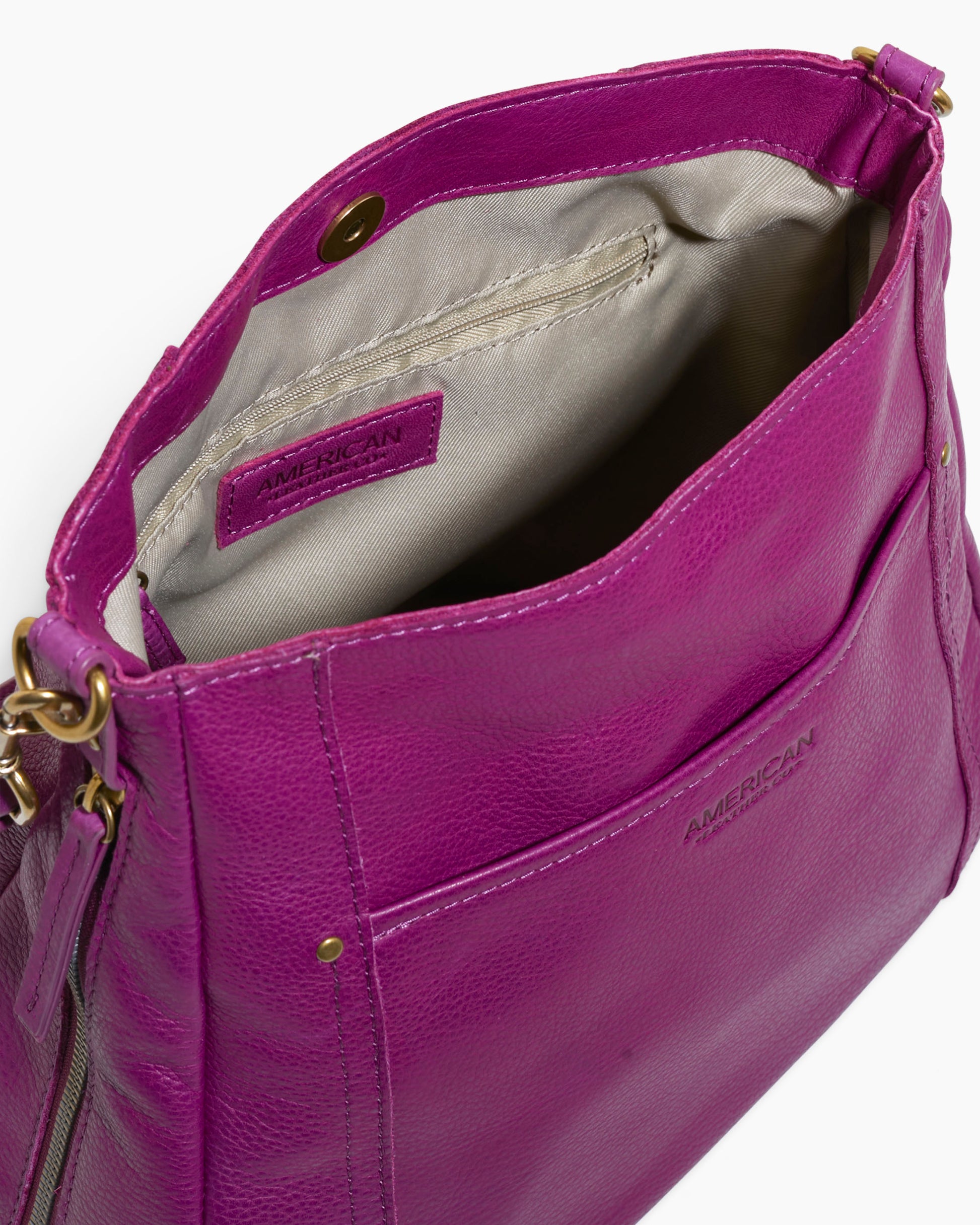 A close-up of an open magenta leather Austin Shoulder handbag with a beige interior. The bag features a zippered inner pocket and an exterior front pocket. The brand name "American Leather Co." is embossed on the exterior front. The bag, crafted from Genuine American Leather, has a brass snap closure and strap rings.