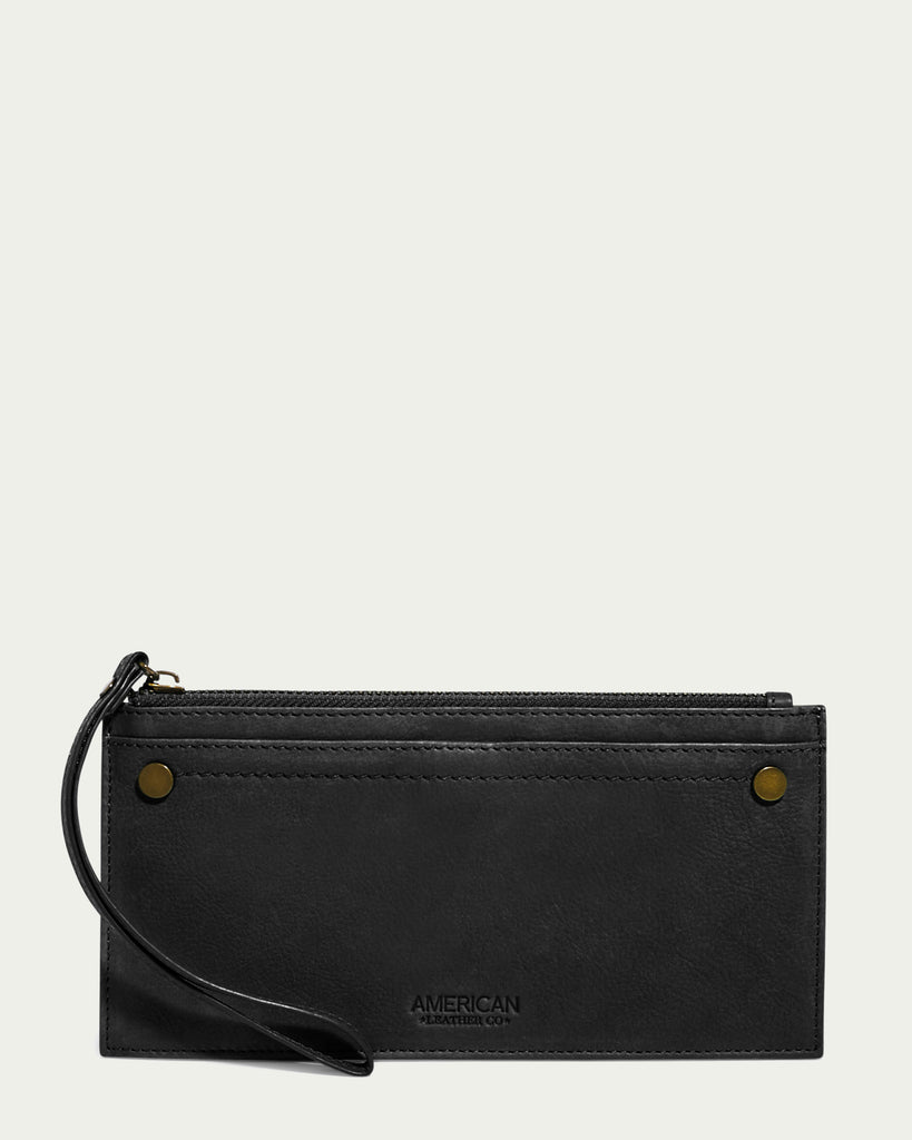 The Bristow CC Zip Wallet Wristlet with RFID by American Leather Co. is a sleek black leather wallet featuring a slim silhouette and rectangular design. It boasts a zipper closure at the top, two small brass rivets on the front corners, and an embossed logo near the bottom center. For easy carrying, it comes with a wrist strap attached to the zipper pull.