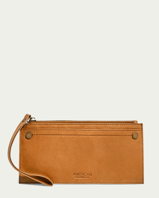 The Bristow CC Zip Wallet Wristlet with RFID from American Leather Co. is a brown leather wristlet featuring a wrist strap on the left side, a zippered compartment on top, and an exterior pocket. Design elements include two metal rivets and an embossed brand logo on the lower front. The background is plain white.