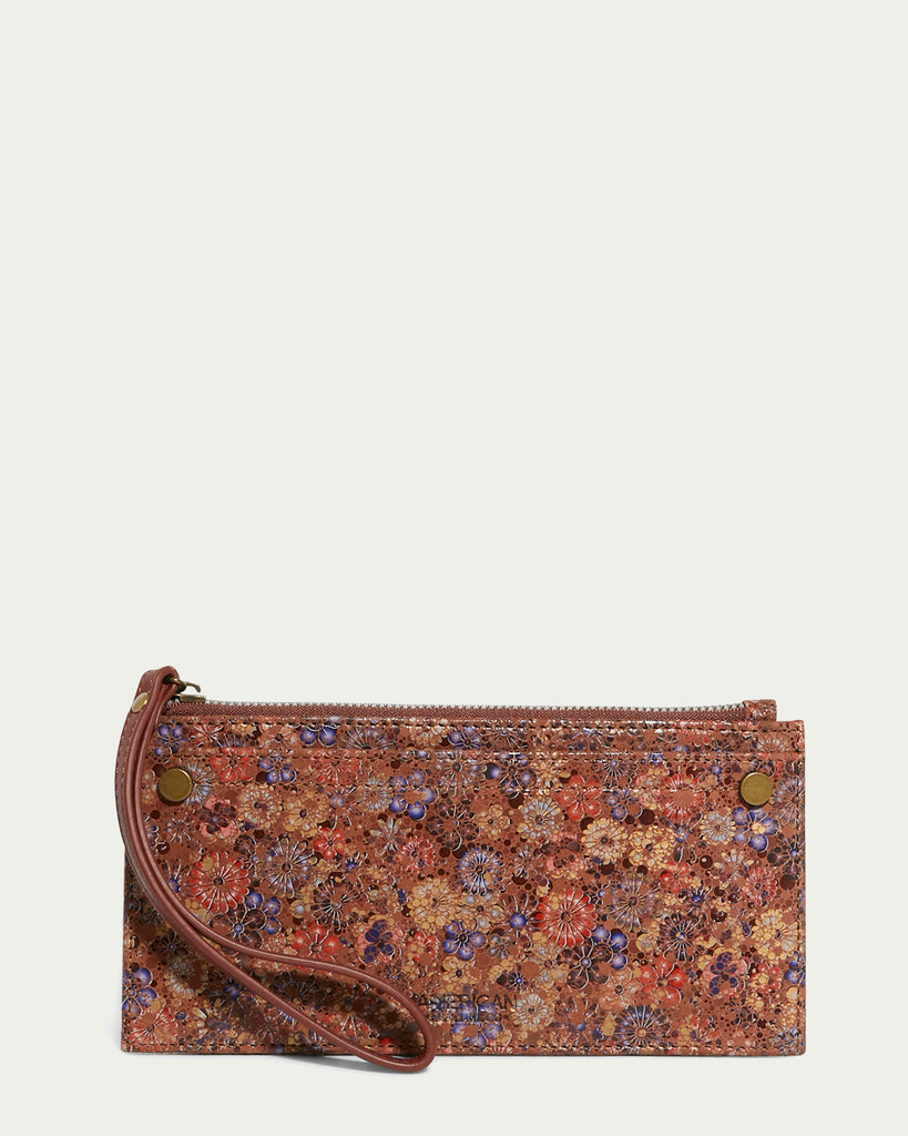 The Bristow CC Zip Wallet Wristlet with RFID from American Leather Co. boasts a floral pattern in shades of brown, orange, and purple. It features two brass snap buttons and a matching wrist strap. This slim wallet wristlet is equipped with a top zipper closure and is displayed against a light beige background.