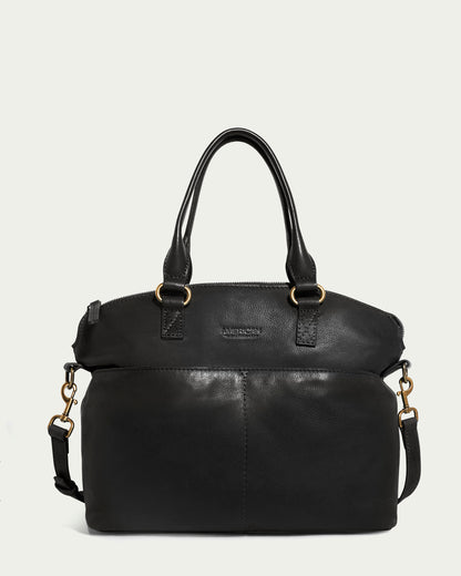 Introducing the American Leather Co. Carrie Dome Satchel, featuring a chic black leather design. This elegant satchel comes with dual handles and an adjustable crossbody strap, showcasing gold-tone hardware and a distinctive front pocket crafted from genuine leather.