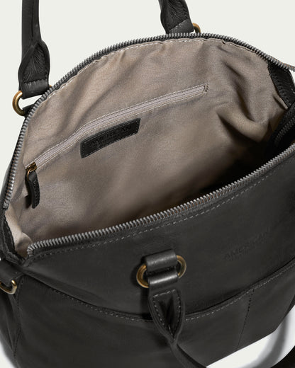 The Carrie Dome Satchel by American Leather Co. is a black genuine leather handbag featuring gold-tone hardware and a sturdy handle. With the top zipper open, it reveals a beige fabric interior complete with a zippered pocket on the side. The bag also includes an adjustable crossbody strap for versatile wear.