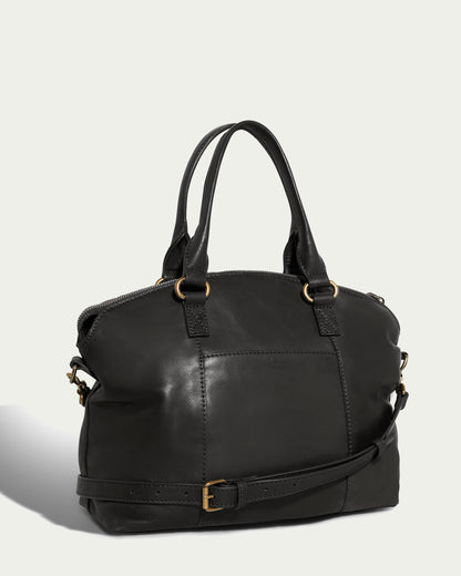 The Carrie Dome Satchel by American Leather Co. is an elegant black leather bag with a structured design, featuring a zippered top, dual handles, and an adjustable crossbody strap. It showcases subtle stitching details and gold-toned hardware set against a light background.