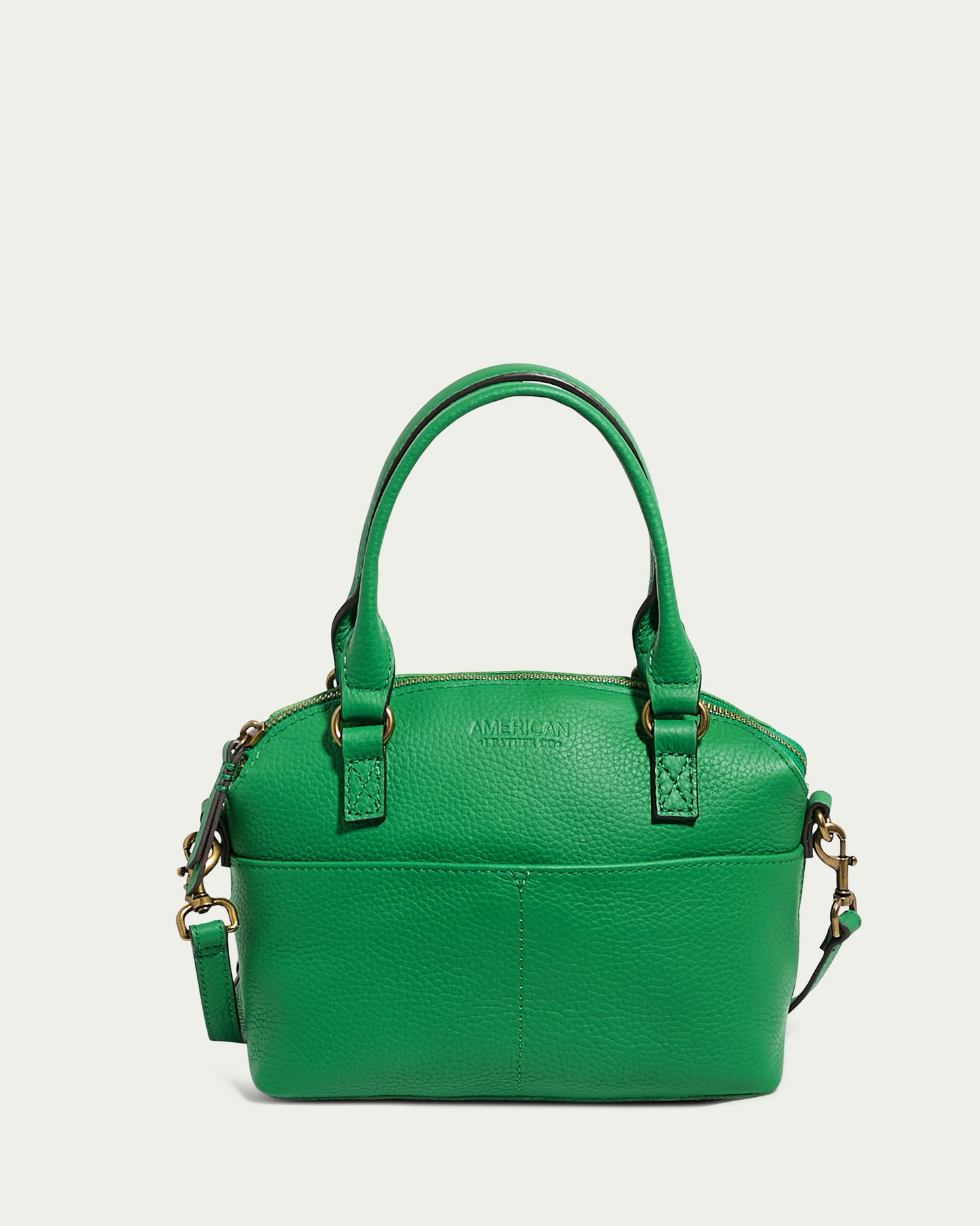 The Carrie Mini Dome Crossbody by American Leather Co. is a compact green leather handbag with a pebbled texture, featuring two short top handles and gold-colored hardware. This genuine leather bag includes a zippered main compartment, a small exterior front pocket, and a detachable shoulder strap.