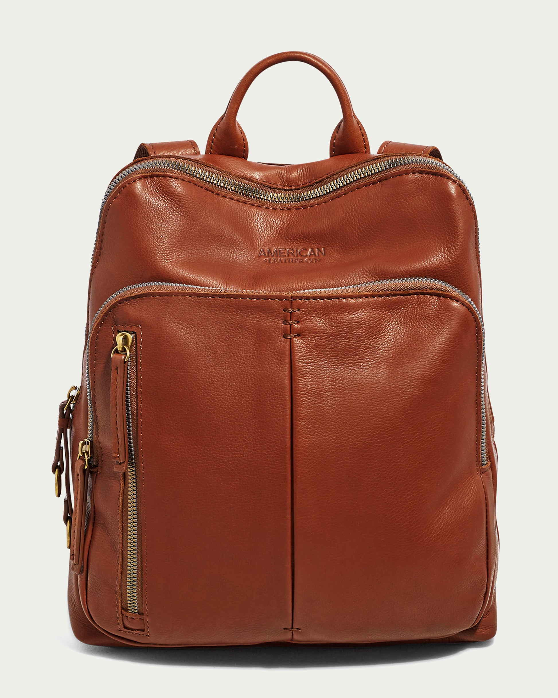 The Cleveland Backpack by American Leather Co. is a genuine brown leather backpack purse with gold zippers. It features a top handle, two adjustable back straps, several zippered compartments, and a main compartment. The quality craftsmanship is evident with "AMERICAN" embossed on the upper front, partially visible.