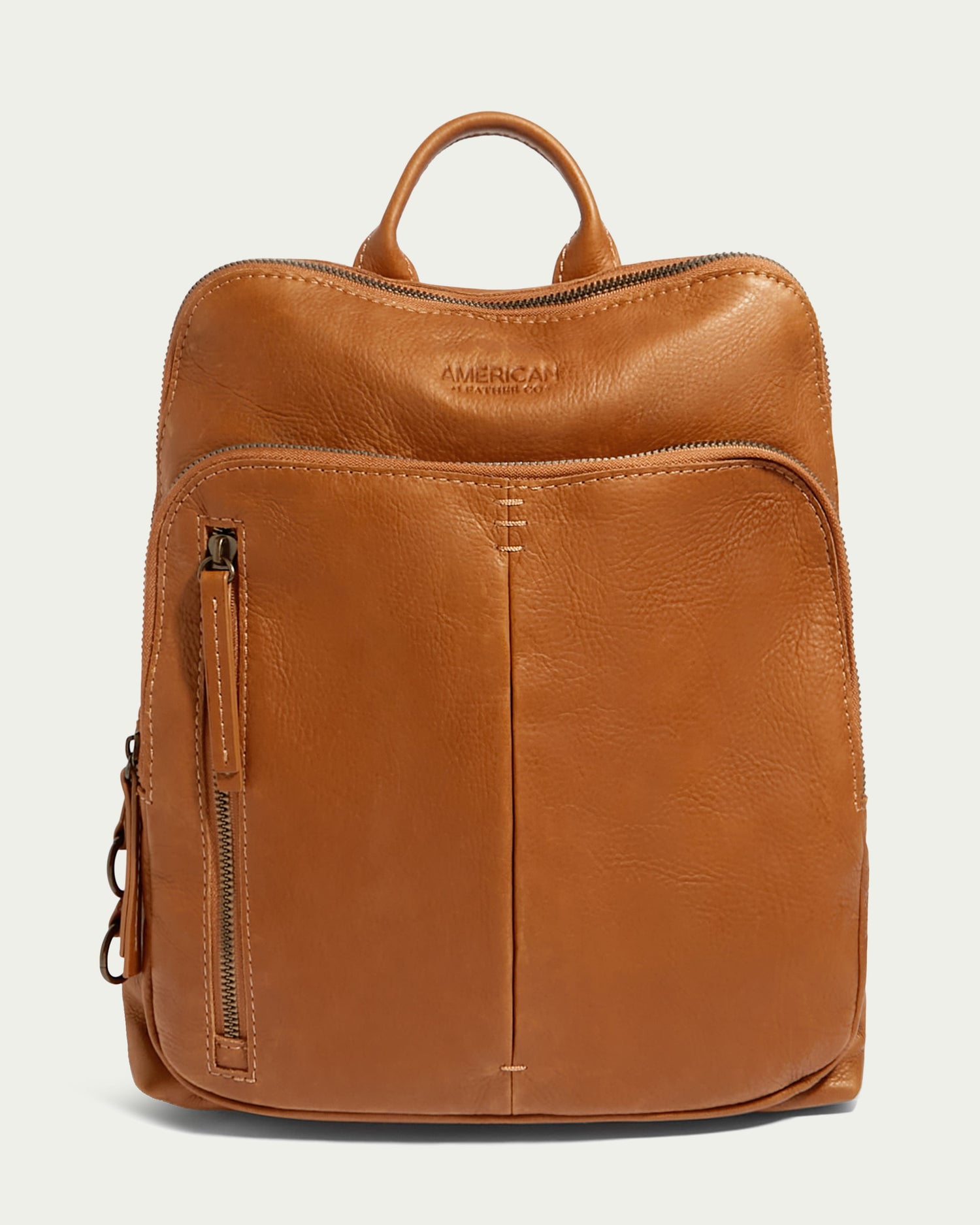 The Cleveland Backpack by American Leather Co. is a tan women's leather backpack made from buttery soft, genuine American leather. It includes a top handle and a front pocket with a vertical zipper on the left side. The brand name "American Leather Co." is embossed near the top of the bag, and the design is minimalist with simple stitching details.