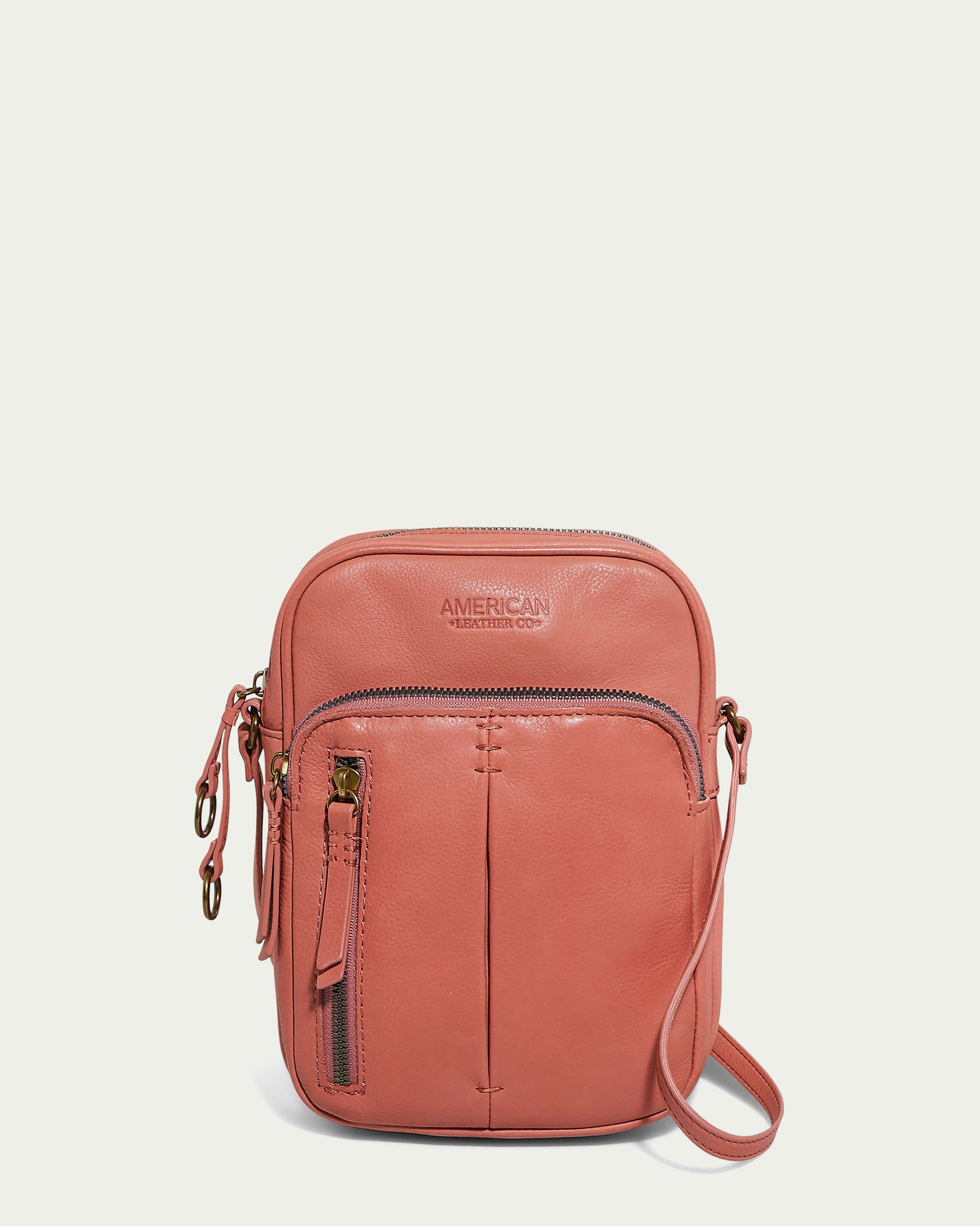 The Cleveland Large NS Crossbody in coral, by American Leather Co., is crafted from genuine American leather and features a front zipper pocket, an adjustable strap, and an embossed brand logo. The gold-tone hardware perfectly complements its simple and compact design.