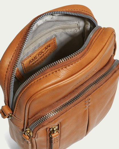 The Cleveland Large NS Crossbody by American Leather Co. is displayed from an angle, highlighting its multiple zippered compartments and a visible brand label inside. Crafted from genuine American leather, its sleek design is accentuated by the smooth glove leather texture and metallic zipper accents on the adjustable strap.