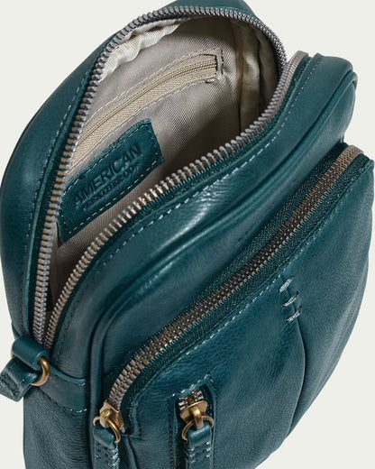 A teal Cleveland Large NS Crossbody bag by American Leather Co. is shown, made from genuine leather with multiple zippered compartments. The top is open to a beige interior and features a unique "American" label. It highlights brass buckles and a textured finish, exuding timeless elegance and functionality.