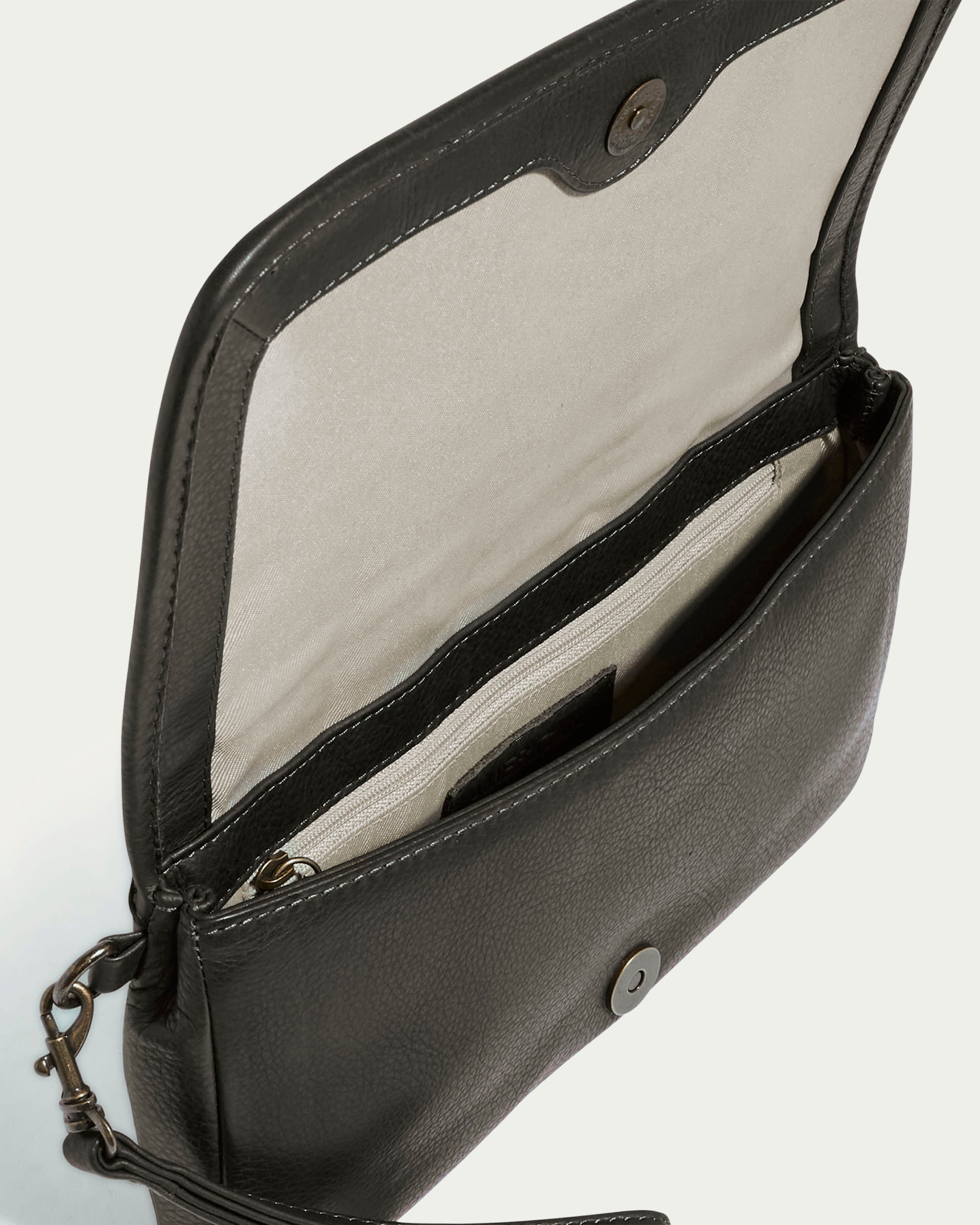 Introducing the Dayton Oversized Clutch by American Leather Co., a black leather shoulder bag that opens to reveal a beige interior crafted from luxurious glove-tanned leather. This sophisticated accessory features vertical panel quilting, a secure snap closure, an interior zippered pocket, and includes a small metal clasp for attaching an optional strap.