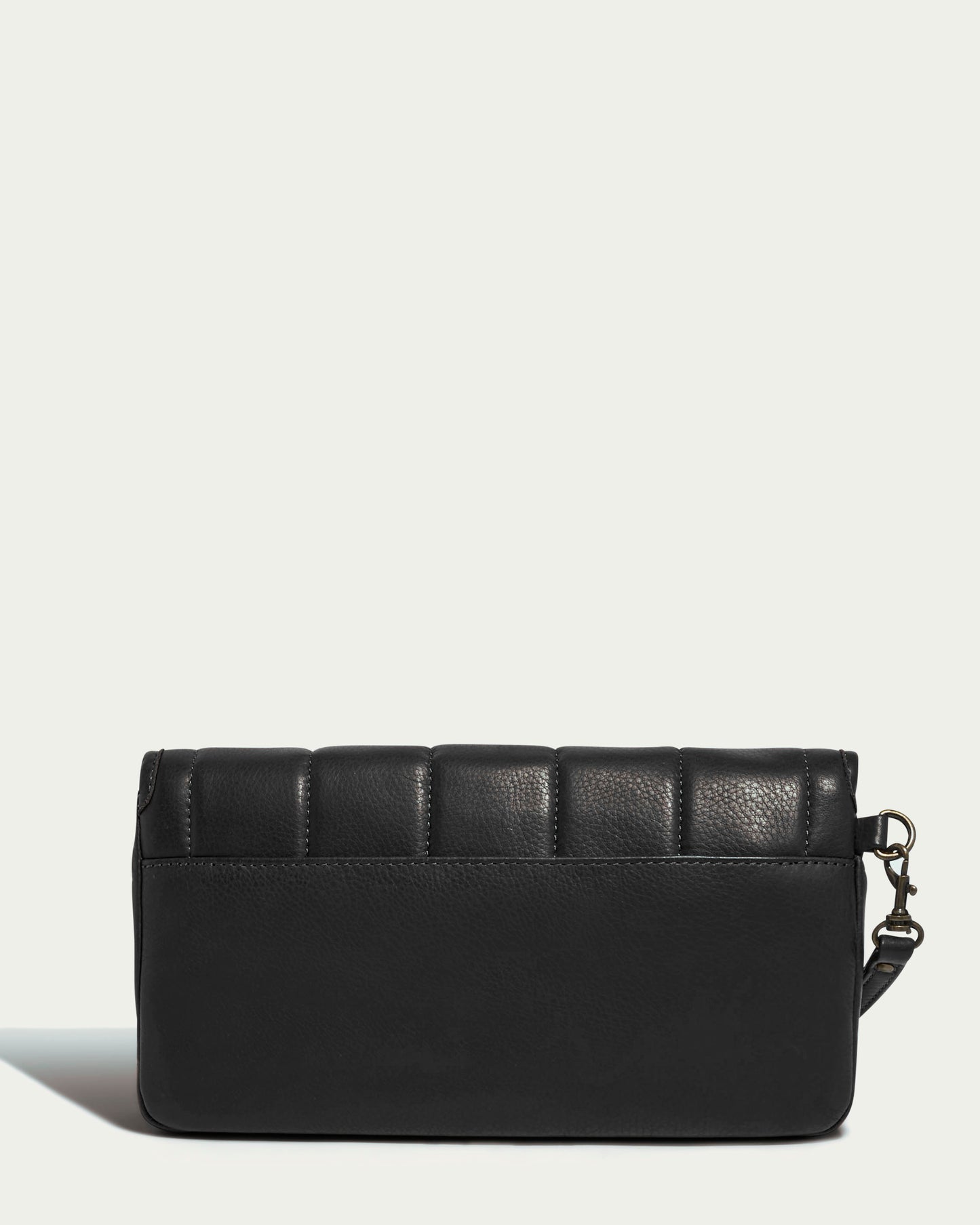 The Dayton Oversized Clutch by American Leather Co. is crafted from black glove-tanned leather and showcases vertical panel quilting along the top edge. It features a detachable shoulder strap, offering a versatility that allows it to transition seamlessly from an oversized clutch to a handbag, all set against a simple, light background.