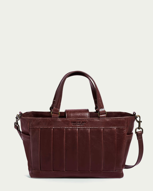 The Mason Mini Satchel Crossbody by American Leather Co. is a dark brown, glove leather handbag with vertical front stitching, featuring two short handles and an adjustable, detachable shoulder strap. Its rectangular shape and antiqued hardware enhance its structured design.