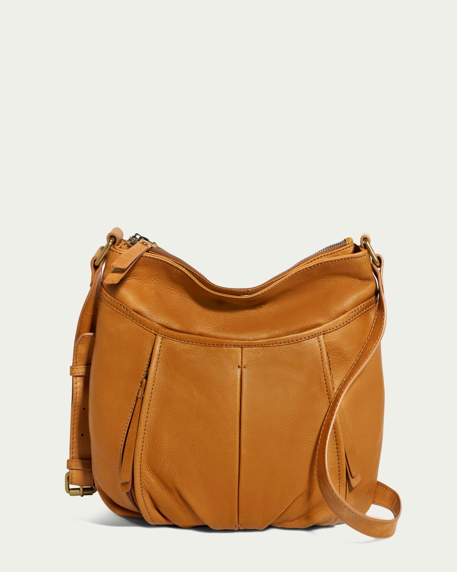 Introducing the Lennie Double Entry Crossbody from American Leather Co., a stylish accessory crafted from tan genuine leather. This bag features a single adjustable strap, zippered top closure, a slightly pleated design, and detailed stitching, making it perfect for wearing as a crossbody against an off-white background.