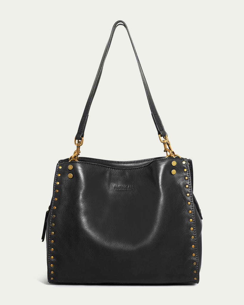 Explore the Lenox Studded Triple Entry Satchel by American Leather Co., a chic black leather handbag made from Genuine American Leather. It boasts gold stud detailing along the sides and gold hardware on the handles, reflecting both a structured shape and luxurious design.