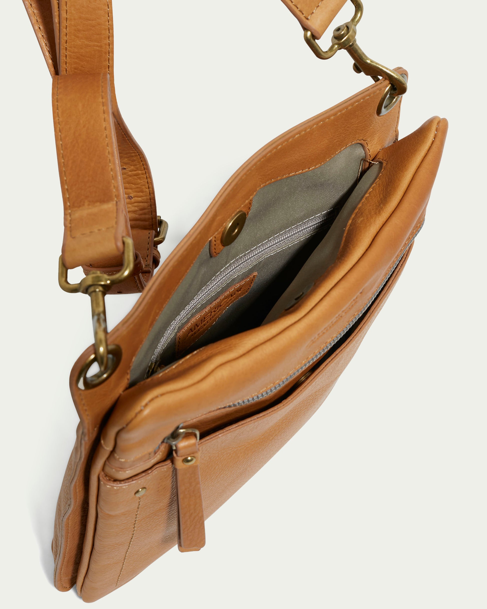 The Lily Multi Compartment Crossbody by American Leather Co. is a fashionable accessory crafted from genuine leather, featuring an open flap with an inside zippered pocket. Its adjustable strap with brass-colored buckles enhances the sleek design and highlights the craftsmanship against a light background.