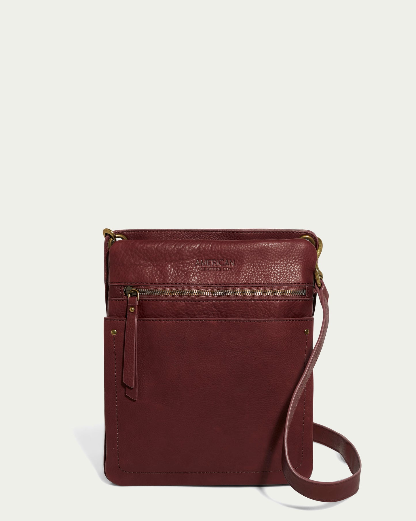 The Lily Multi Compartment Crossbody by American Leather Co. is a maroon genuine leather accessory with two front zippered pockets, elegant gold-tone hardware, and a comfortable strap, set against a light gray background for stylish versatility.