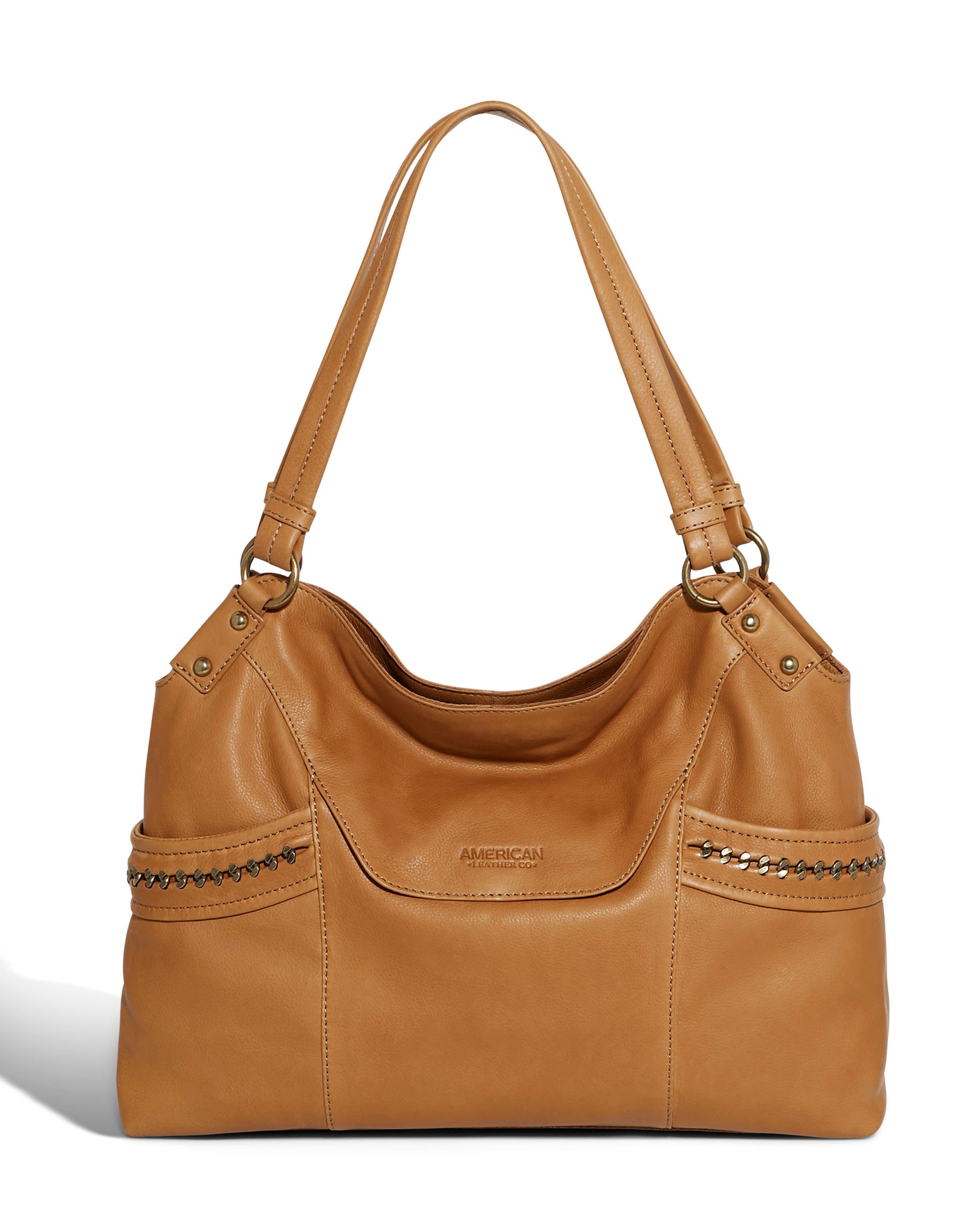 The Sumner Satchel by American Leather Co. is an elegant handbag made from genuine light brown leather, featuring shoulder straps, decorative metal studs, multiple pockets, and detailed stitching. It also includes a subtle embossed brand logo in the center for added style.