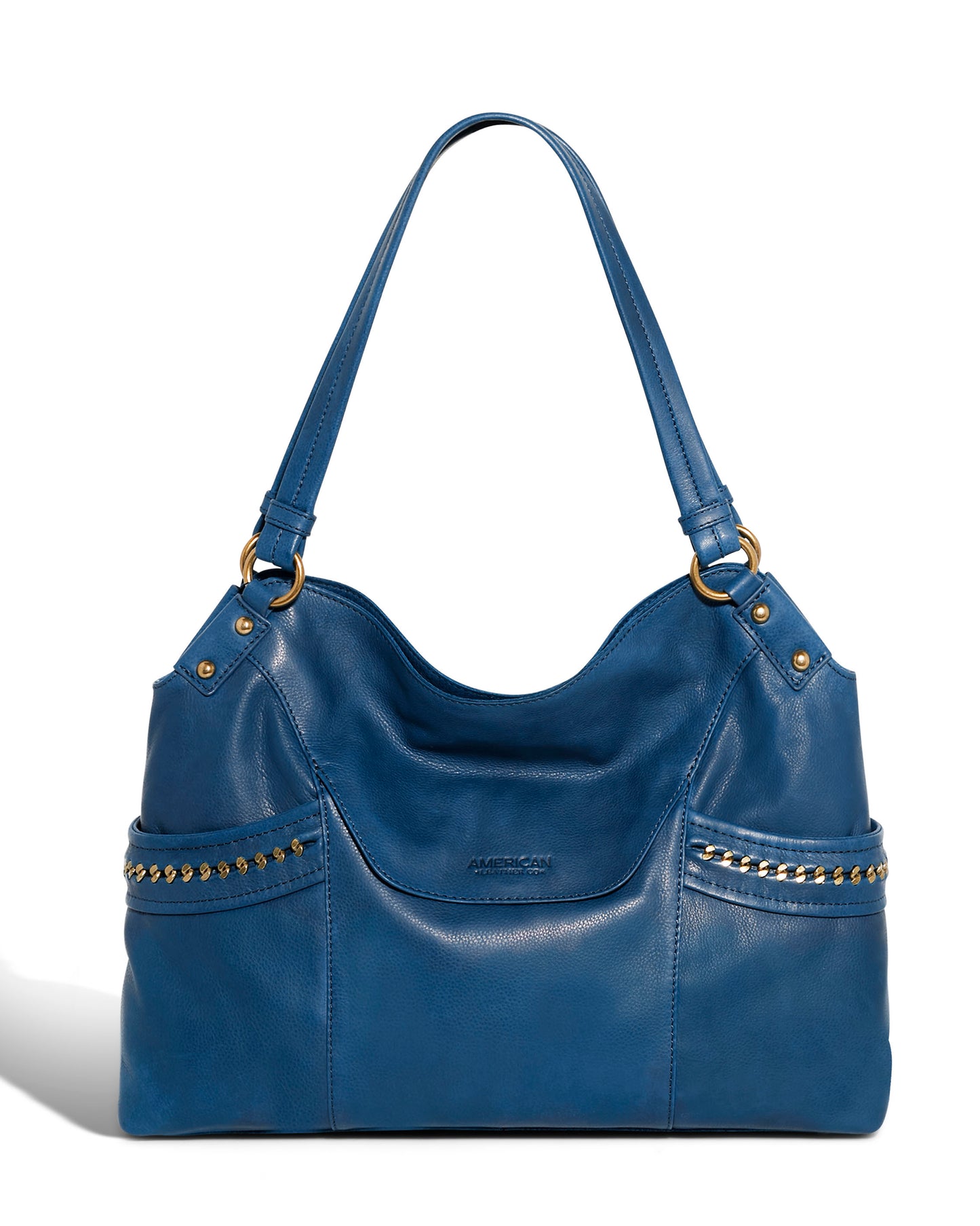 The Sumner Satchel from American Leather Co. is crafted from genuine leather and showcases a blue color with gold stud embellishments. It boasts a smooth texture, a roomy interior, two shoulder straps, and side pockets adorned with studded accents.