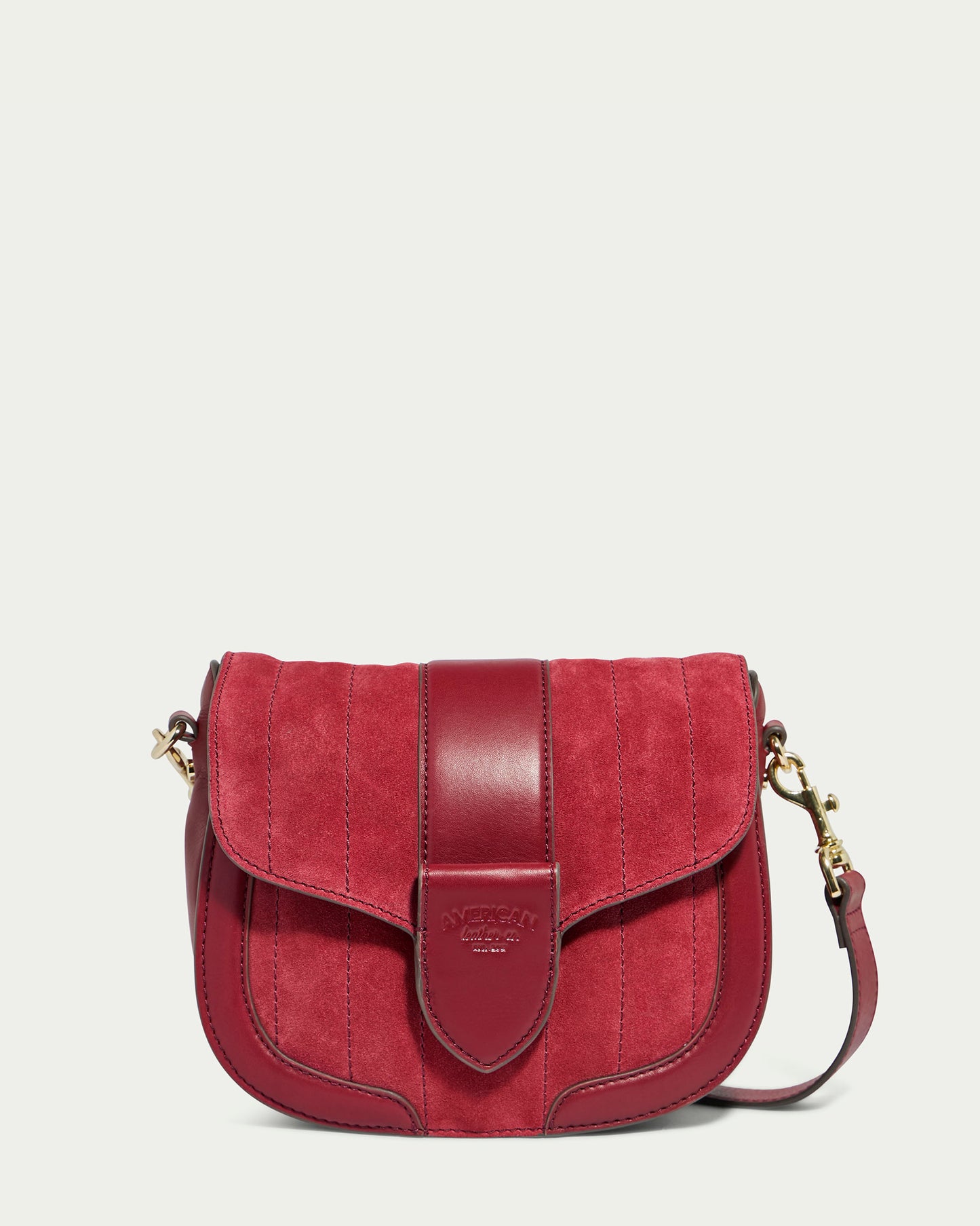 Introducing the Aiken Flap Crossbody by American Leather Co., a stylish red suede shoulder bag with quilted stitching. This elegant accessory features a flap closure with a smooth leather strap and gold-tone clasp. It also comes with an adjustable, detachable leather shoulder strap adorned with gold-tone hardware on both sides, showcasing impeccable genuine leather craftsmanship.