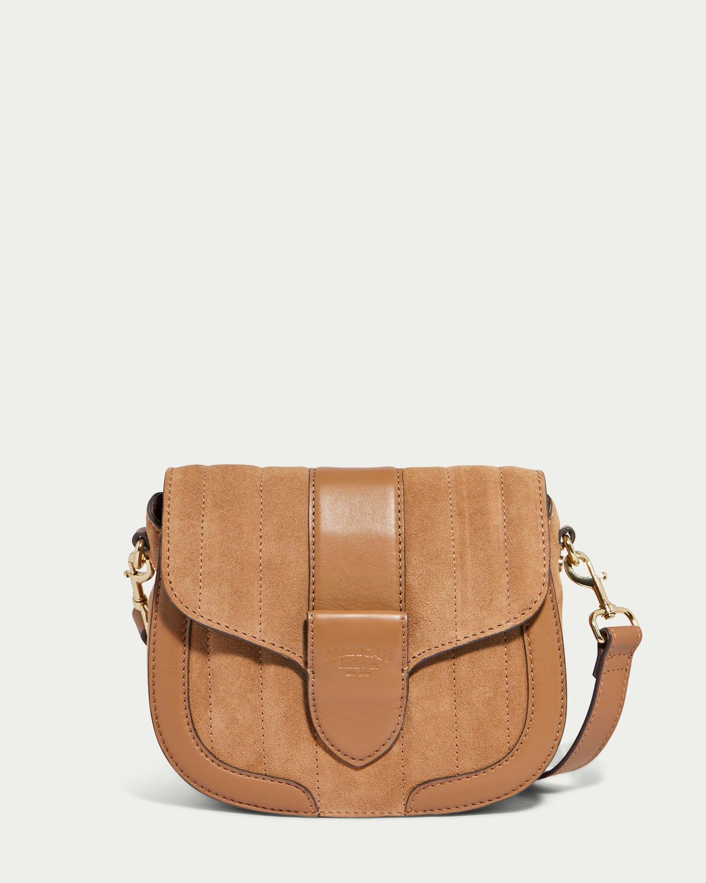 The Aiken Flap Crossbody from American Leather Co. is a tan leather crossbody bag featuring a front flap closure, decorative stitching, and an adjustable shoulder strap. Made from genuine leather, it showcases gold-tone hardware, including a clasp and strap attachments, and has a smooth texture.