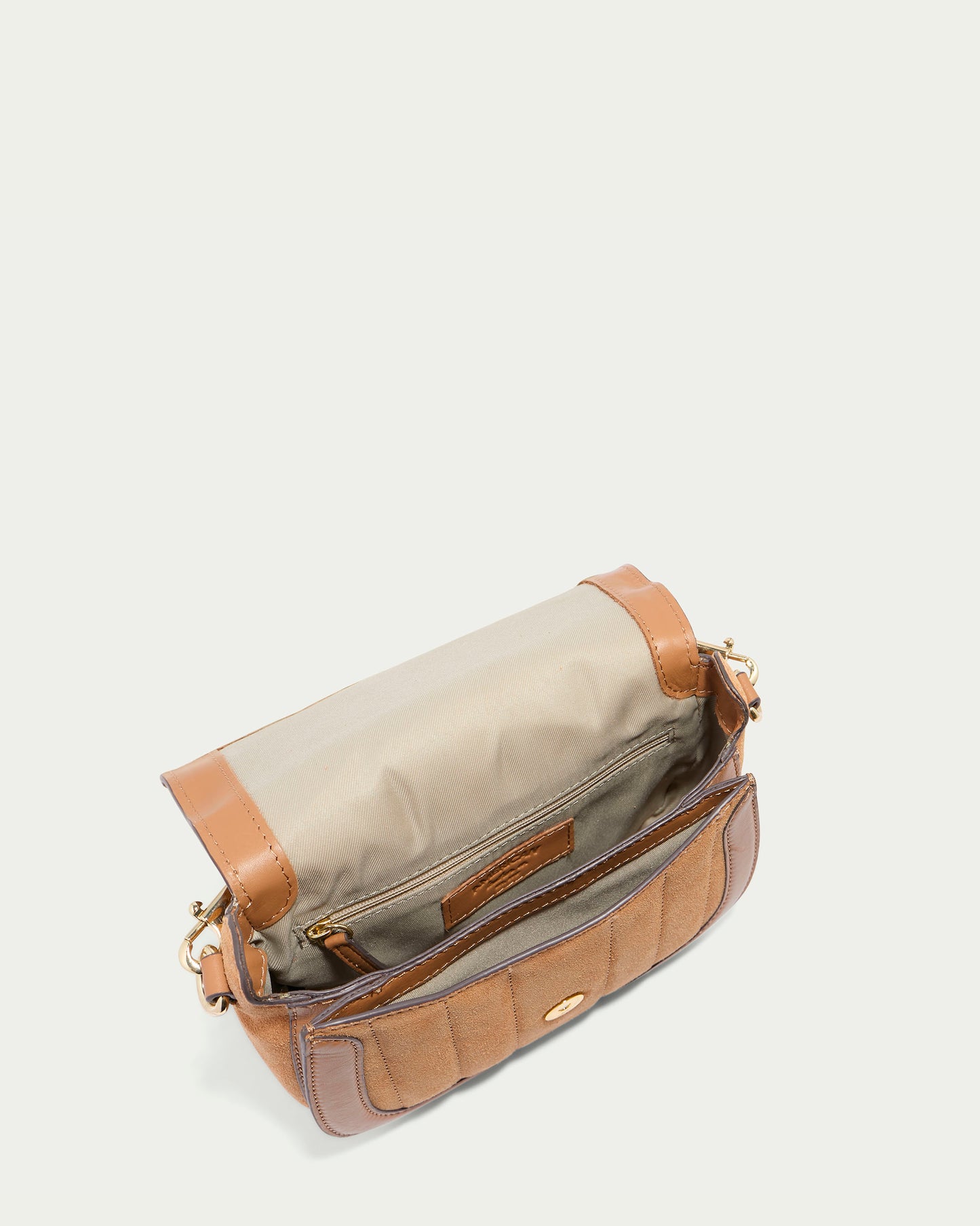 The Aiken Flap Crossbody by American Leather Co. is open, showcasing its beige interior lining. This small handbag, featuring a tan and brown color scheme, includes a front pocket, gold hardware, and an adjustable shoulder strap. Crafted from genuine leather with suede details, the bag is presented against a plain white background.