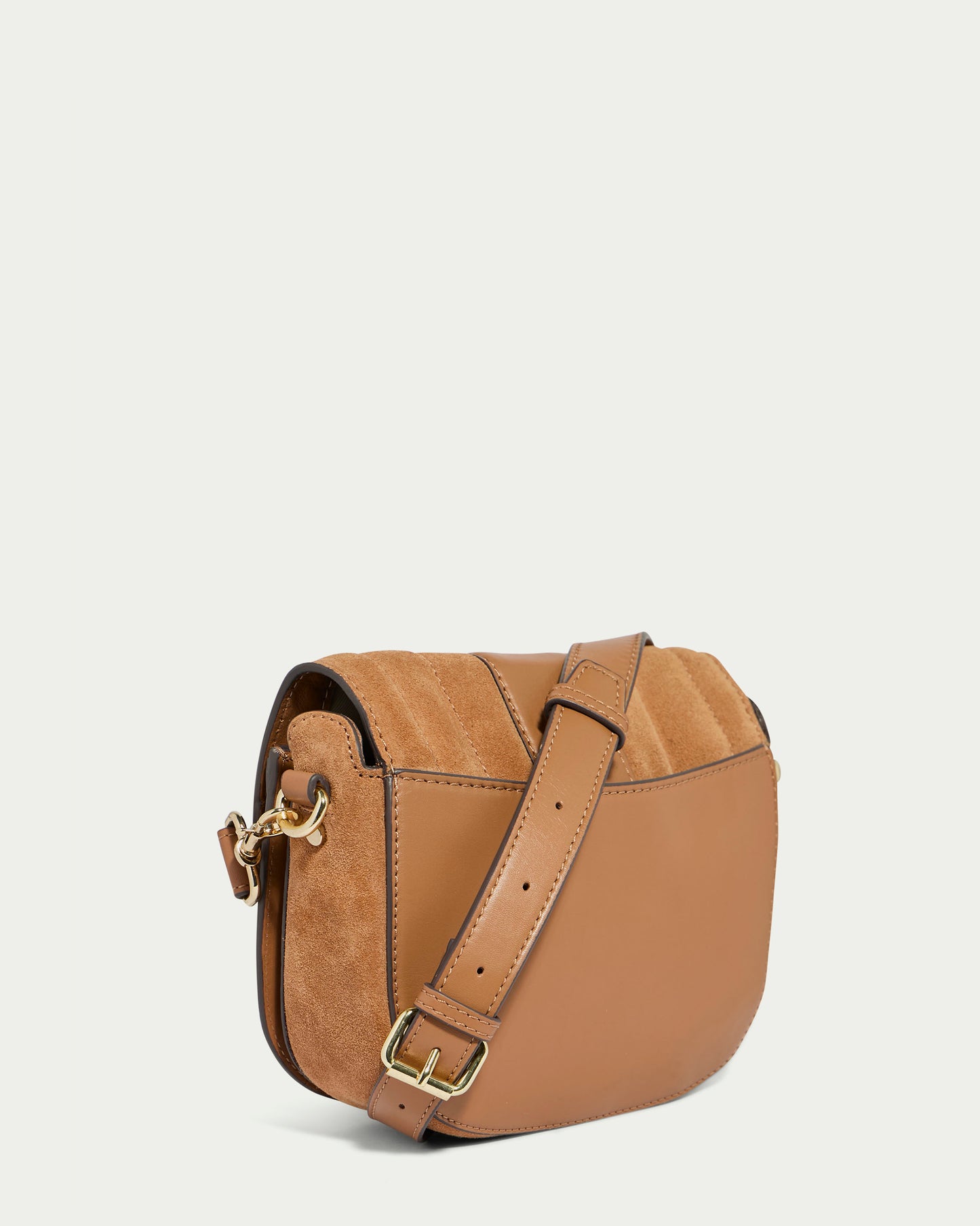 The Aiken Flap Crossbody by American Leather Co. is a brown bag made from genuine leather, featuring a quilted pattern on the top flap and subtle suede details that elevate its elegant design. The crossbody bag includes an adjustable strap with a gold-tone buckle and a matching clasp on the side, all set against a solid off-white background.