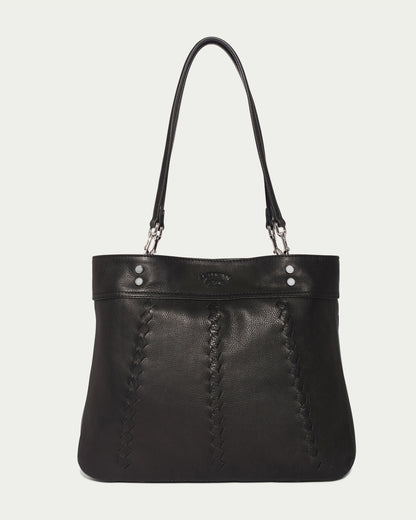 The Alpine Triple Compartment Tote by American Leather Co. is a stylish black leather handbag featuring two shoulder straps and a genuine leather exterior. The bag showcases intricate stitched detailing along the front in a vertical pattern, accented with two silver rivets and a small embossed logo at the top. The background is white.