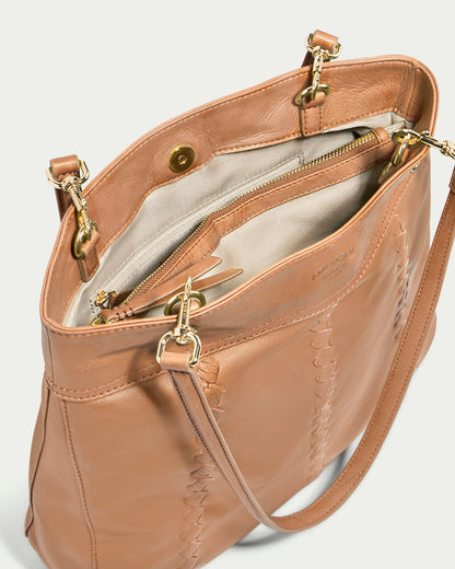 The Alpine Triple Compartment Tote by American Leather Co. is a tan genuine leather handbag featuring gold hardware and an open top. Inside, it boasts three compartments, including one with a zipper. The exterior showcases intricate stitching details, and the bag comes with a detachable shoulder strap equipped with gold clasps.