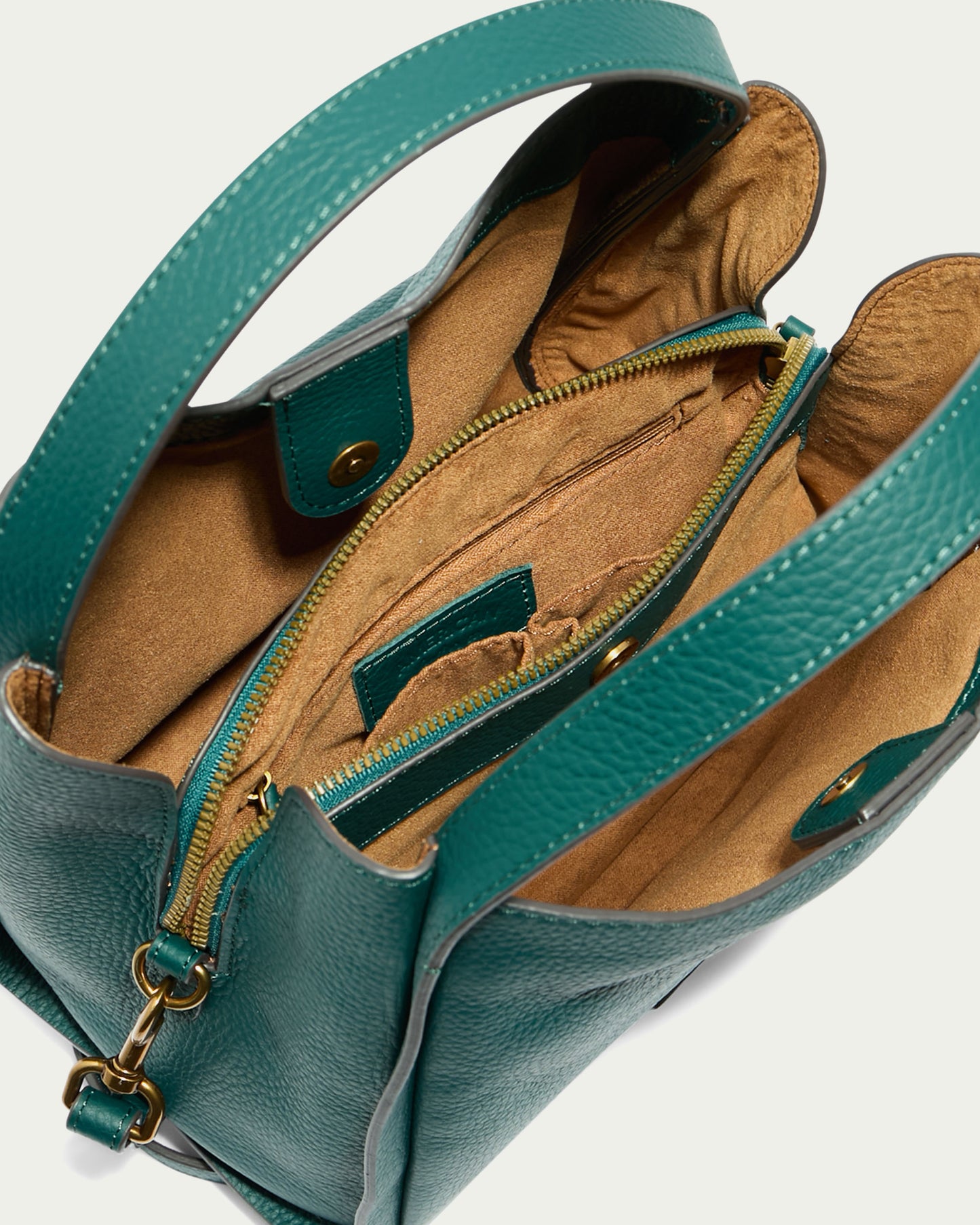 The Auburn Triple Compartment Convertible Crossbody by American Leather Co. is displayed open, showcasing its interior with tan lining. This teal, weather-proof leather handbag features multiple compartments, including a zippered pocket, an open pocket, and a central zippered section. Made from genuine leather, it has two sturdy handles and gold-tone hardware.