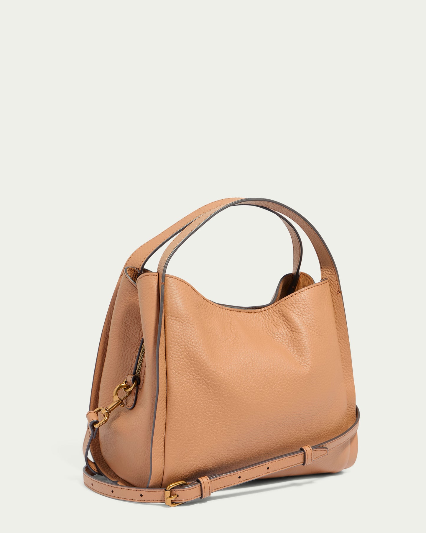 The Auburn Triple Compartment Convertible Crossbody by American Leather Co. is featured against a plain background. This tan-colored genuine leather handbag boasts a soft, pebbled texture, a curved top, a single handle, and an adjustable crossbody strap attached with gold-tone hardware.