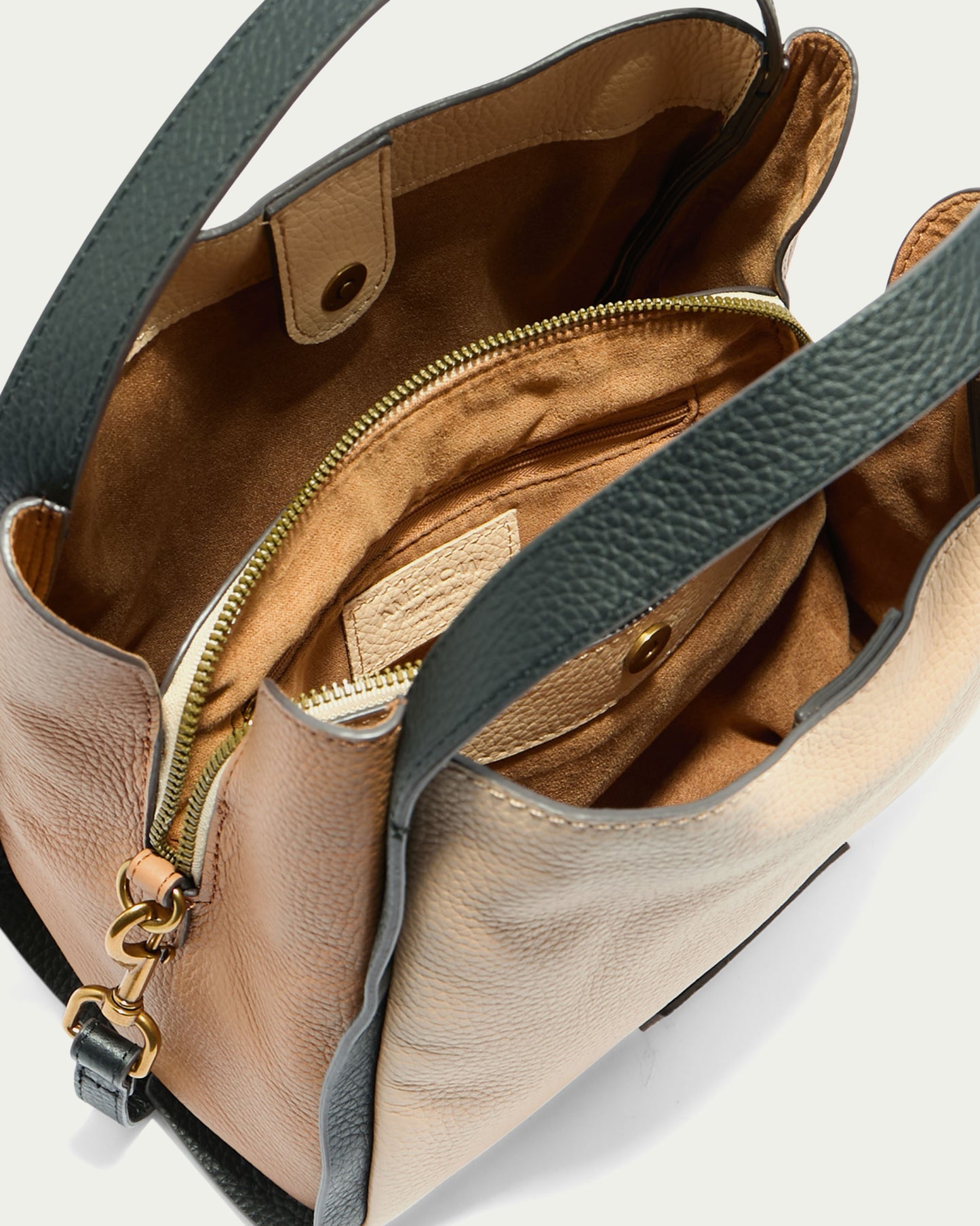 A close-up view inside the weather-proof Auburn Triple Compartment Convertible Crossbody from American Leather Co. reveals a stylish beige and green genuine leather handbag. It features an open top with a partial snap closure, an interior zippered pocket, and light brown interior lining.