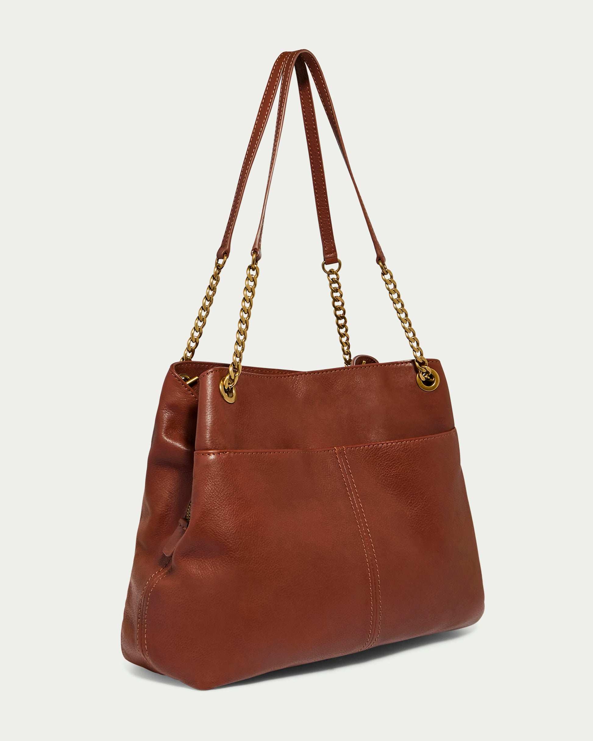 The Brisben Chain Shopper by American Leather Co. is crafted from genuine leather in a rich brown shade and features gold chain shoulder straps for added elegance. The bag boasts a smooth texture and minimalist design, with lightweight chains that attach using circular metal rings. This triple-entry shopper is photographed against a plain, light background for maximum visual appeal.