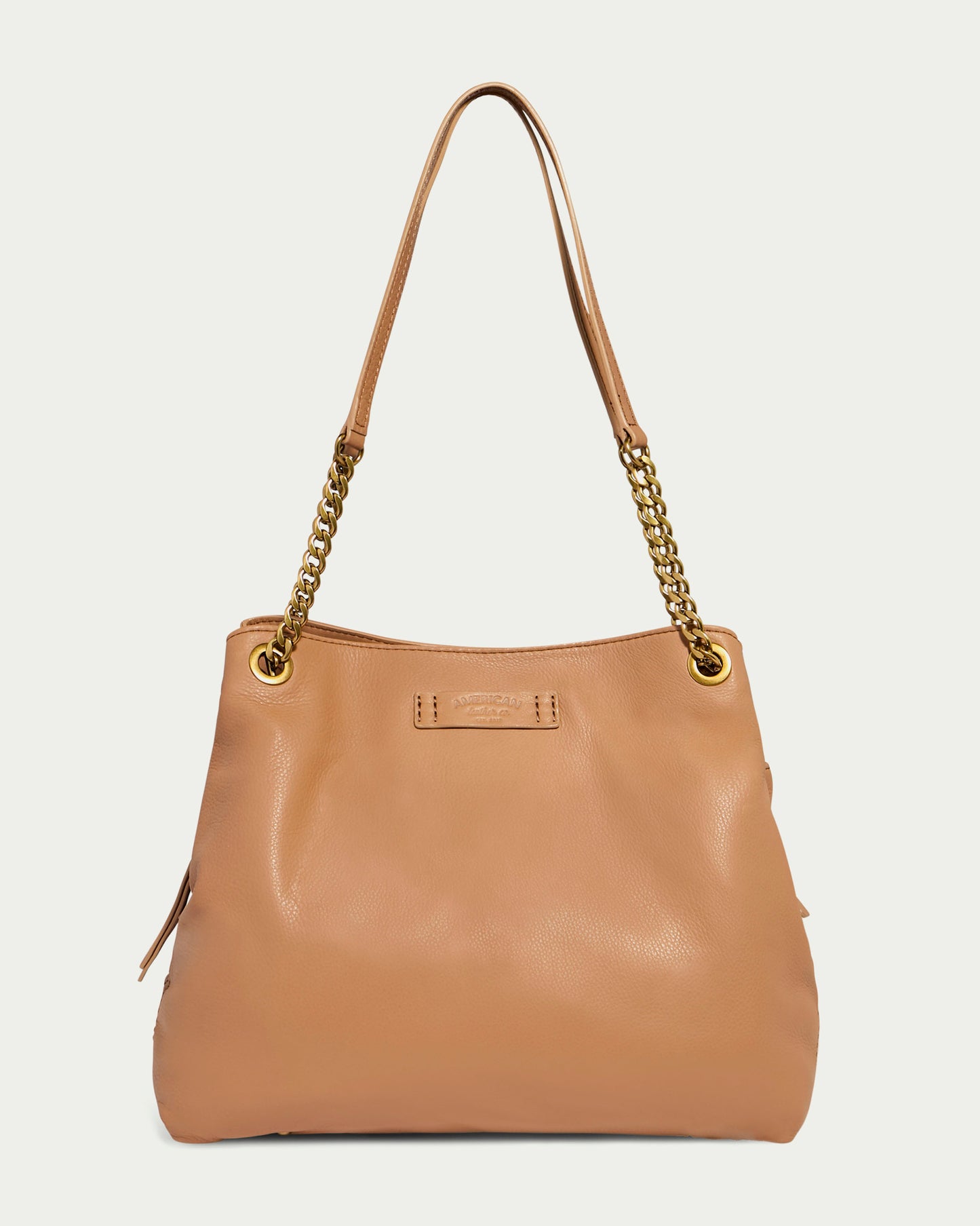 The Brisben Chain Shopper by American Leather Co. is a tan Genuine Leather Shopper bag featuring lightweight gold chain straps and gold eyelets at the attachment points. The design is simple and rectangular with subtle stitching along the edges, and it sports a small logo plate on the upper front center.