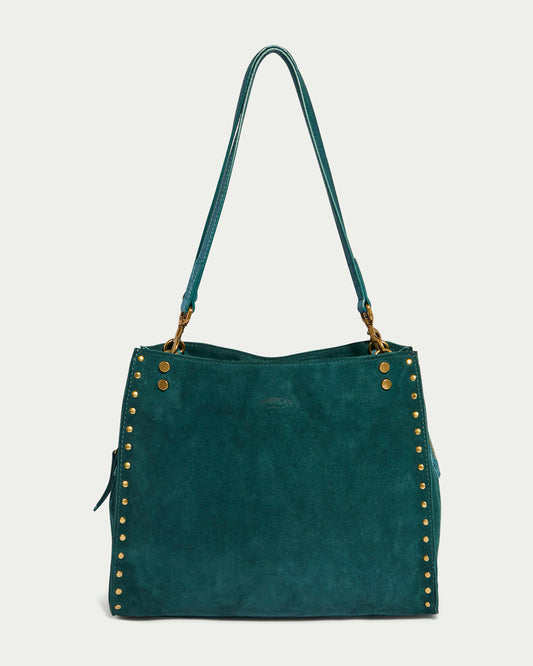 The Lenox Studded Triple Entry Satchel by American Leather Co., crafted from Genuine American Leather, features elegant stud detailing along its edges. This teal suede handbag boasts dual shoulder straps and a rectangular shape with a slightly slouchy appearance.