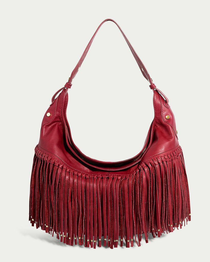 The Lilly Ziptop Hobo by American Leather Co. is a bohemian-style red leather handbag featuring a single shoulder strap and fringe details along the bottom. Made from genuine leather, it showcases metal accents at the base of each fringe strip against a plain, light-colored background.