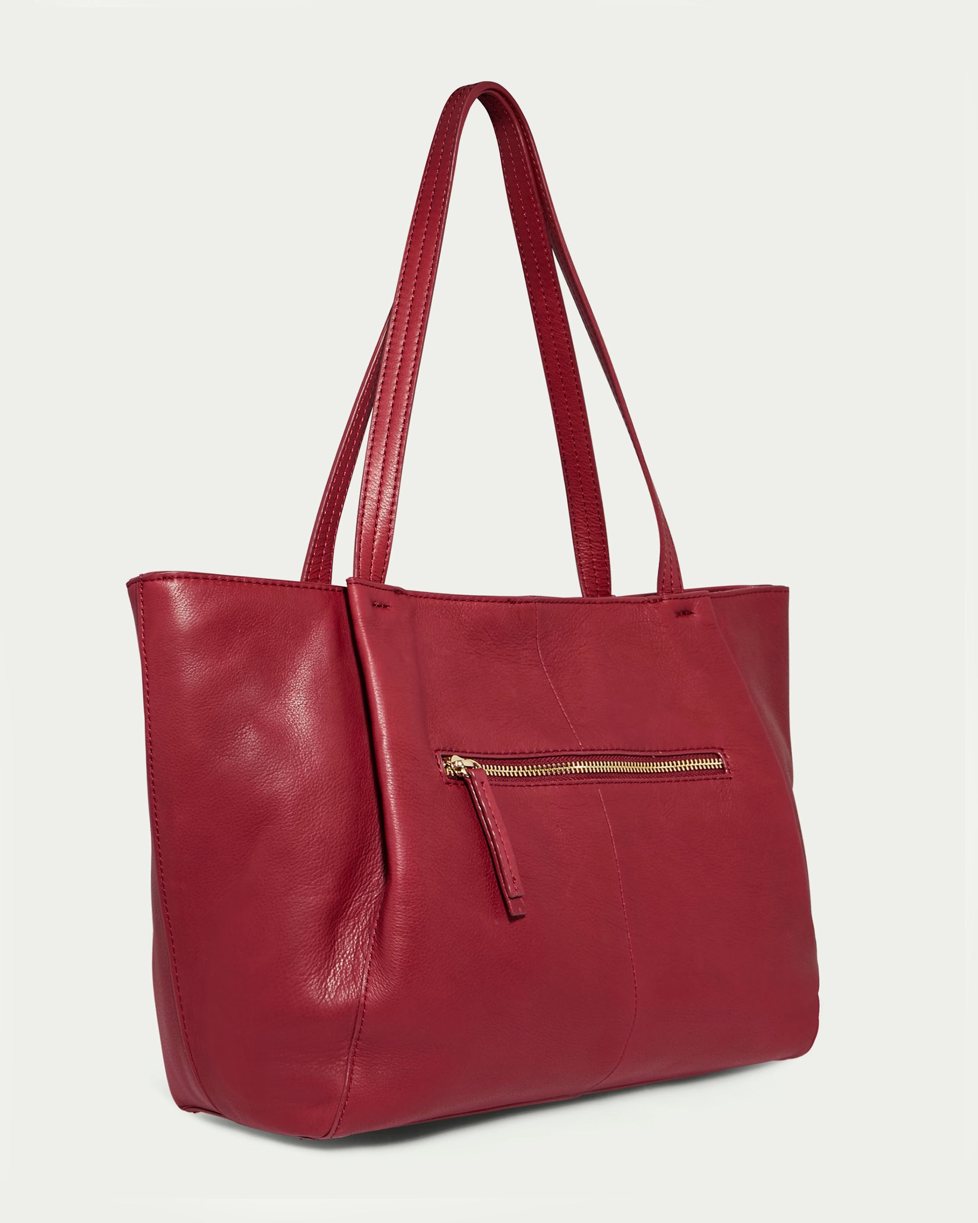 The Lindley Tote by American Leather Co. is a spacious, oversized deep red fashion tote made from genuine leather. Featuring long shoulder straps, a sleek design, and a front zippered pocket with a gold zipper, this bag's smooth and slightly shiny finish adds an elegant touch.