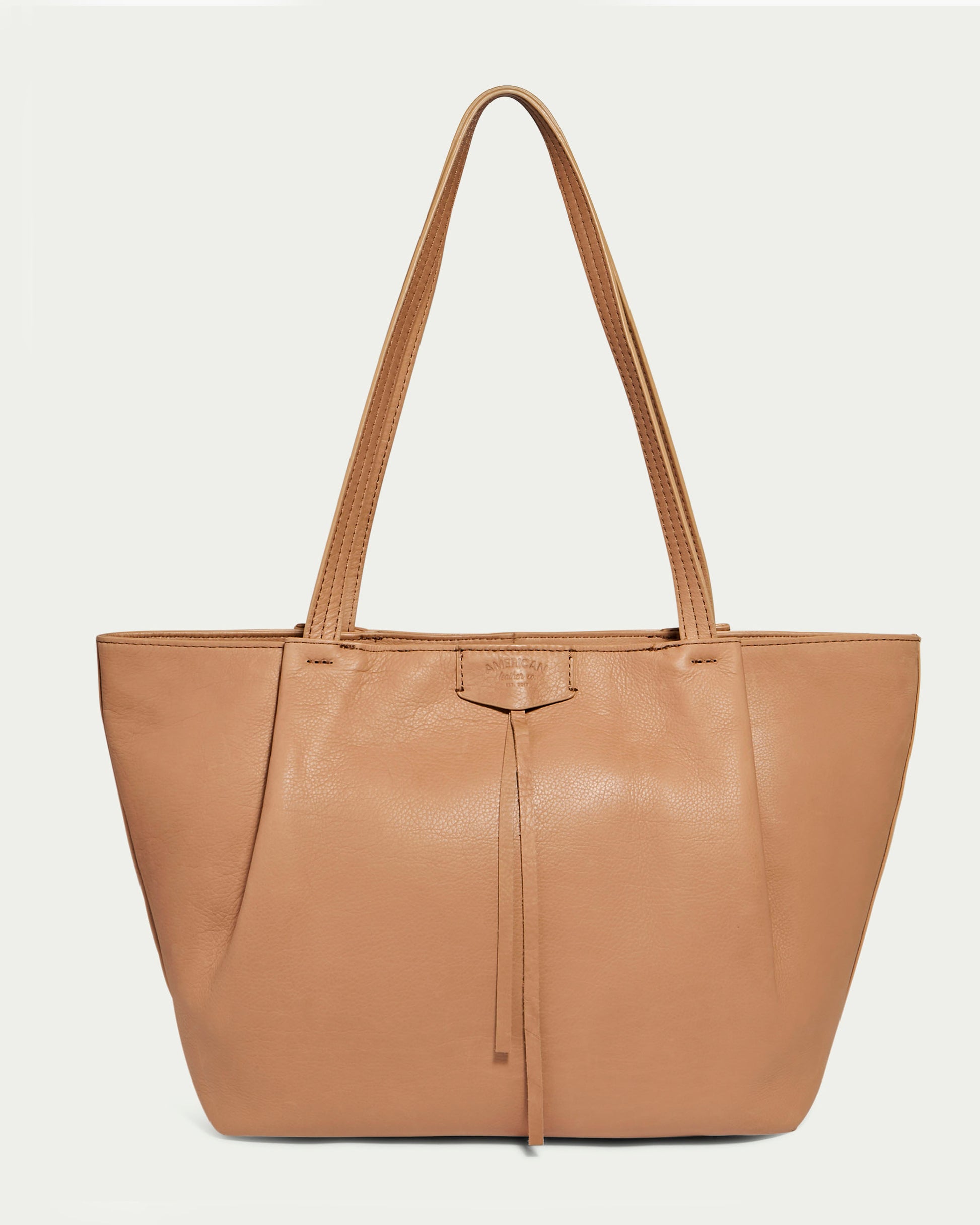 Introducing the Lindley Tote by American Leather Co., a genuine leather, tan oversized tote bag featuring two shoulder straps and a smooth texture. The bag boasts a minimalist design with subtle stitching, a central leather accent, and a top zipper closure. Its simple, elegant appearance makes it suitable for everyday use and is showcased beautifully against a plain white background.