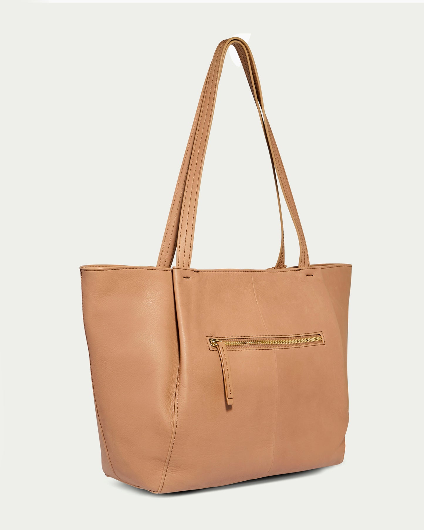 The Lindley Tote by American Leather Co. is a tan leather tote bag featuring a straightforward design with two long handles, a top zipper closure, and a front zipper pocket. The background is light grey.